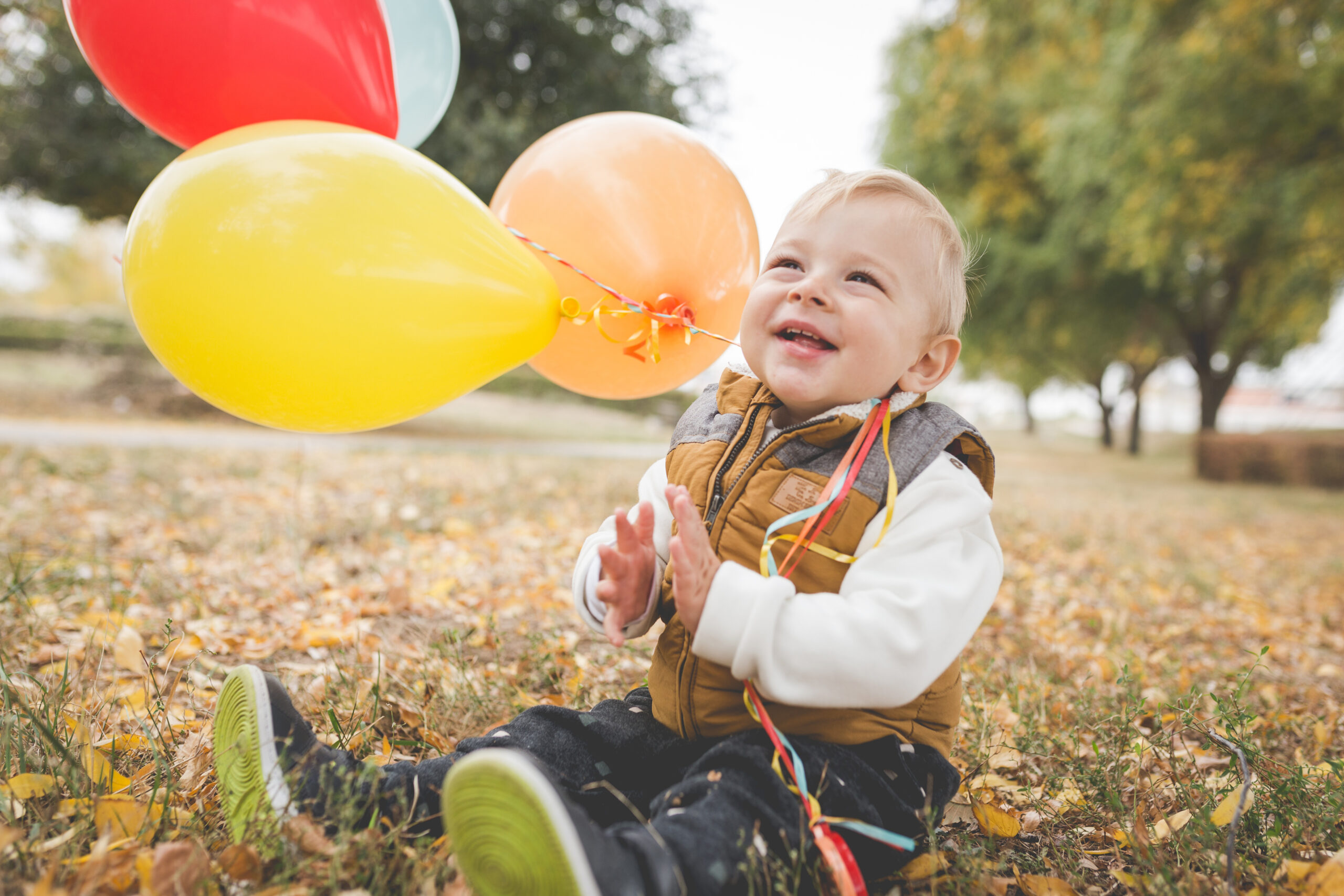 Happy male toddler playing with balloons in the park
