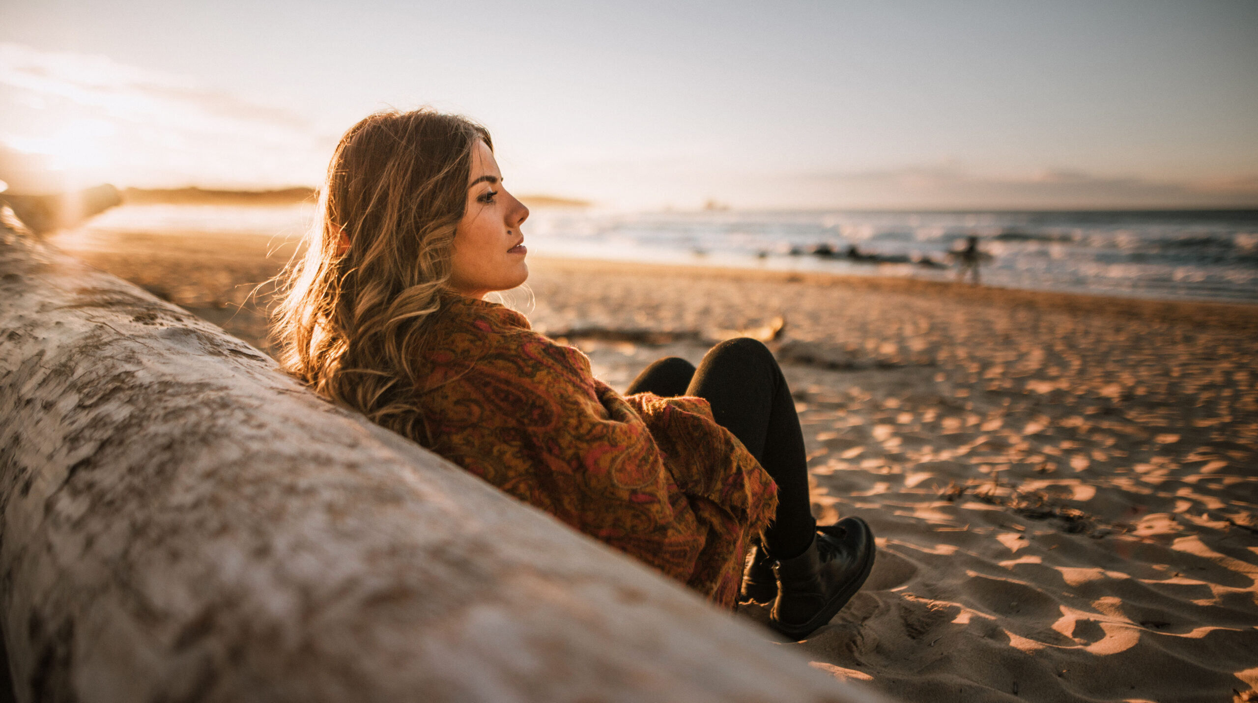 Young woman sitting by a beach at sunset in winter