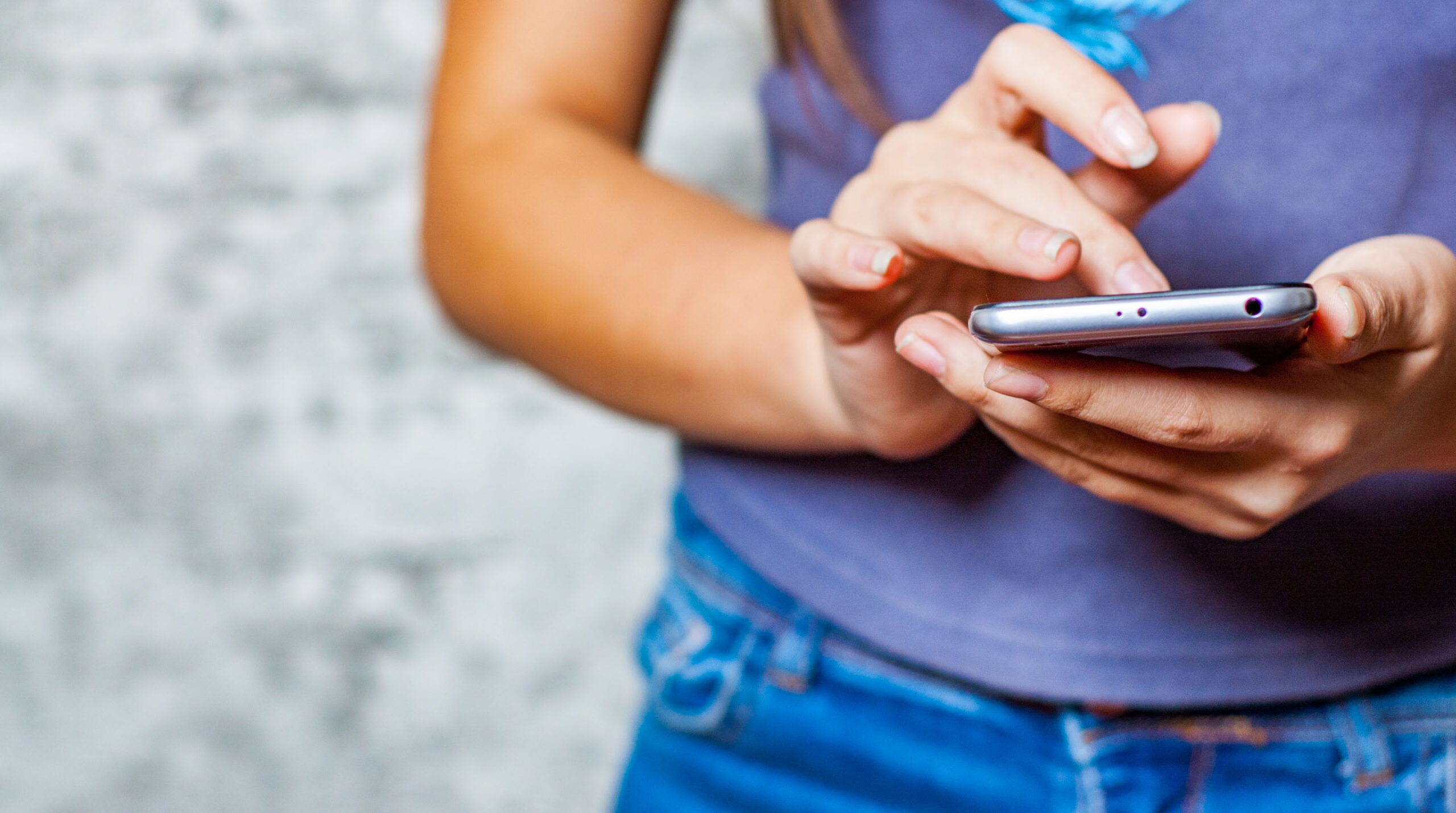 young teenager girl hand using mobile phone or smartphone on gray wall background
