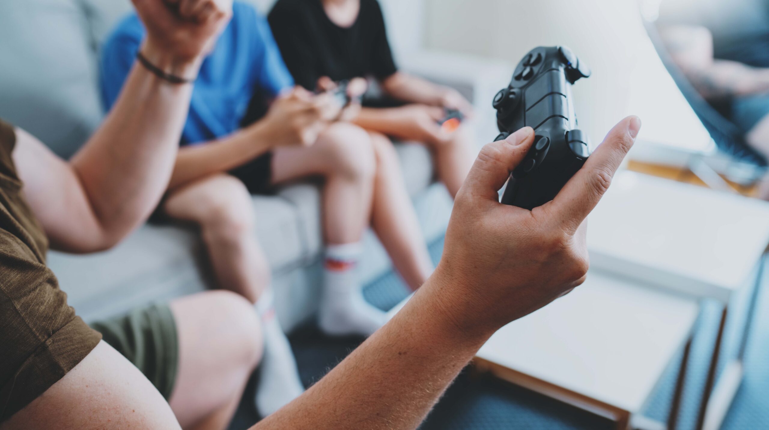 Young best friends sitting on a sofa in living room and playing video games. Family relaxing time at home concept. Cropped.