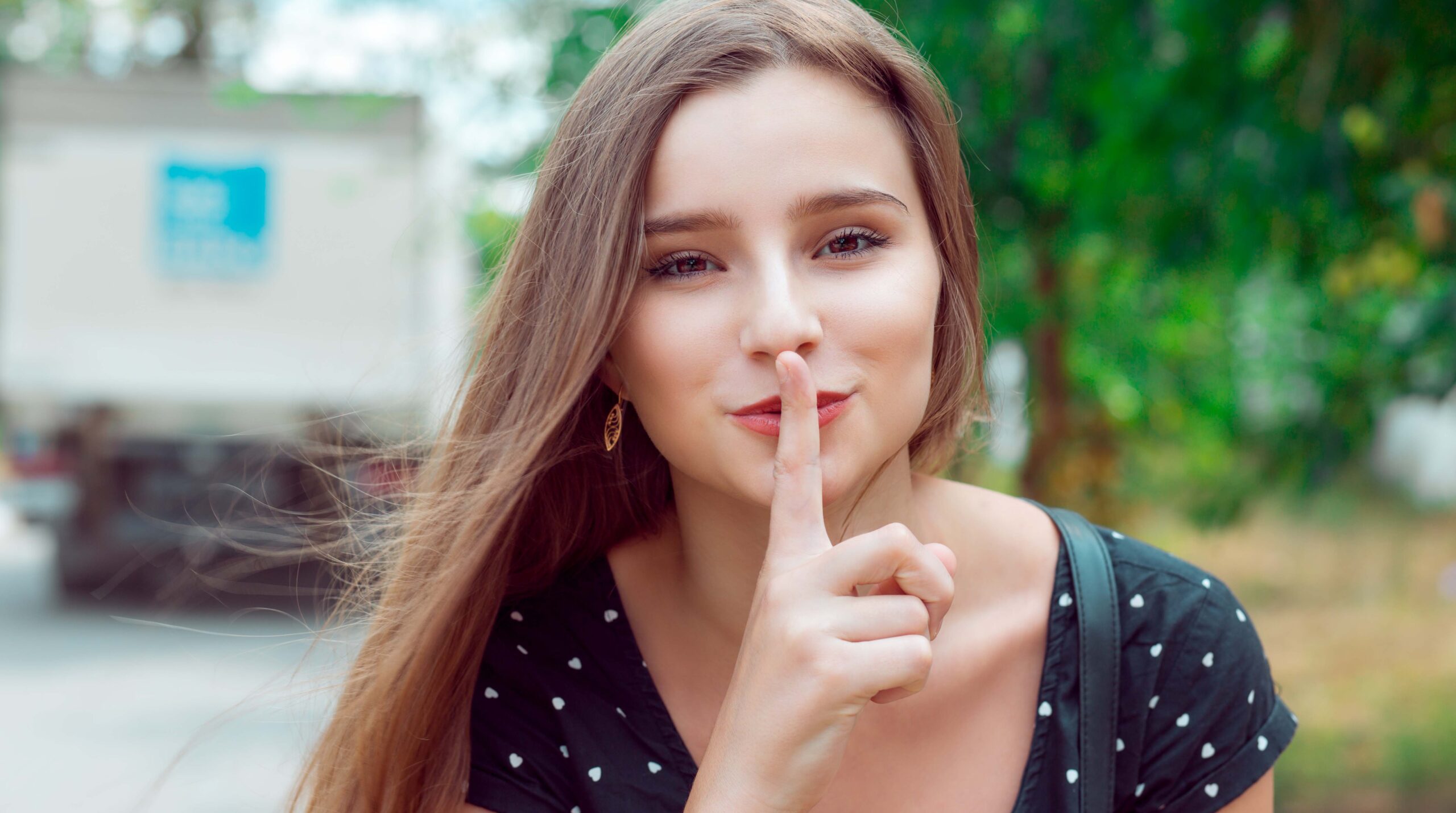 Woman asking for silence or secrecy with finger on lips hush hand gesture city park