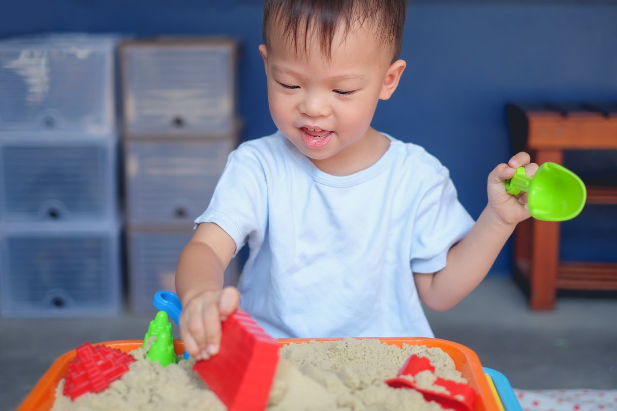 Cute smiling Asian 2 - 3 years old toddler boy playing with kinetic sand in sandbox at home / nursery / day care
