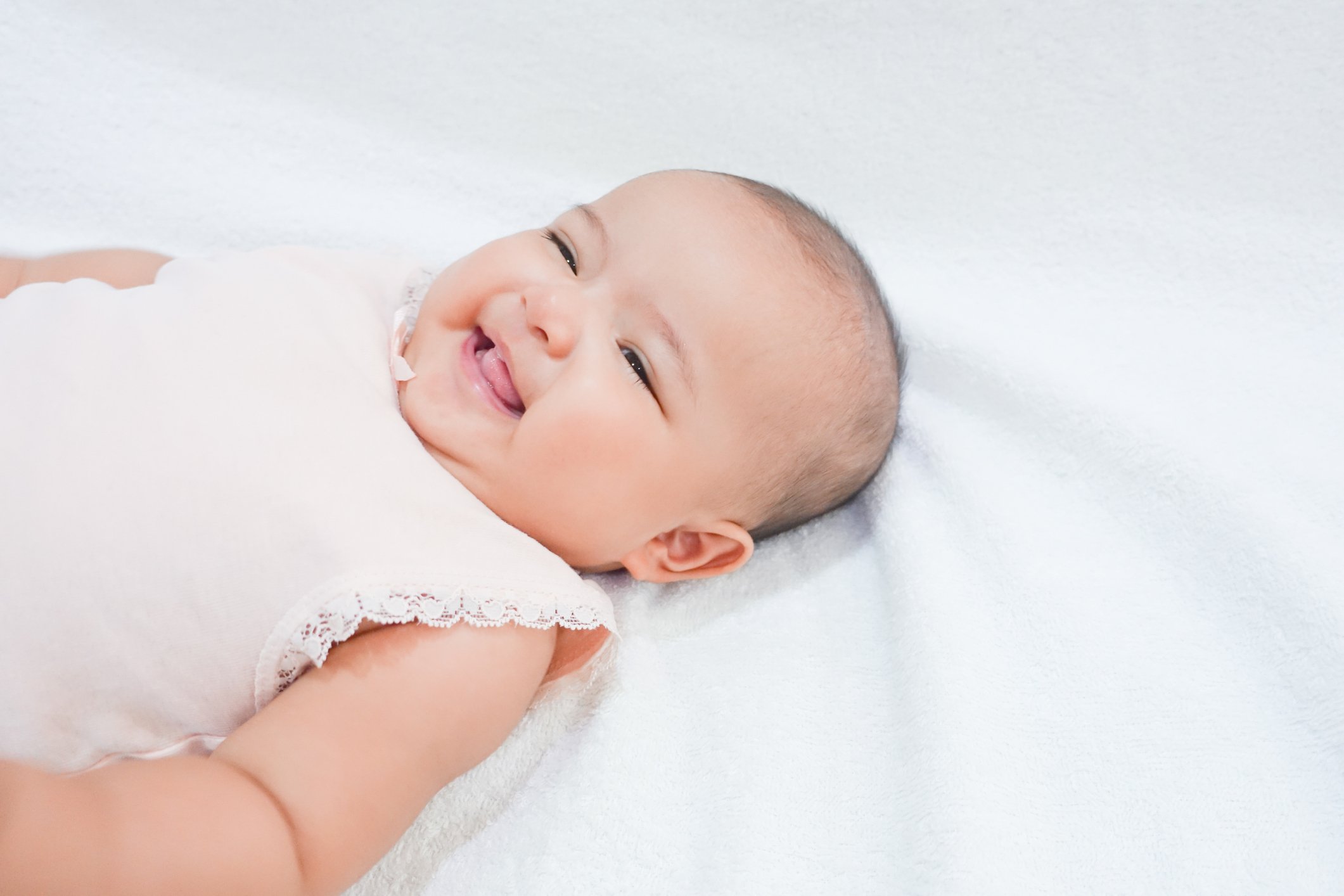 Happy Asian newborn baby girl put her hand up in the air with beautiful smile on white towel background.