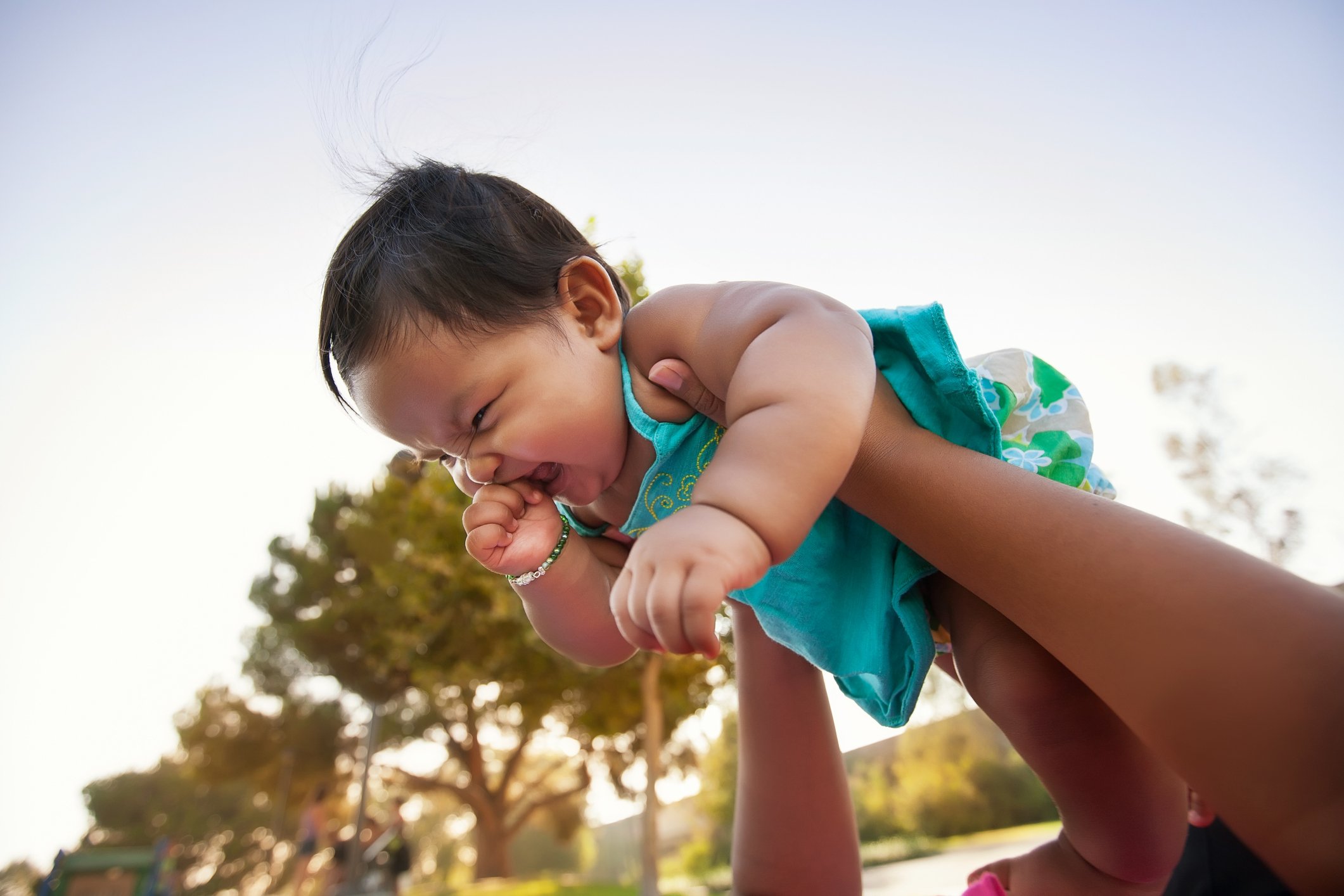 Baby girl being lifted up by mother into the sky, baby looks excited and nervous.