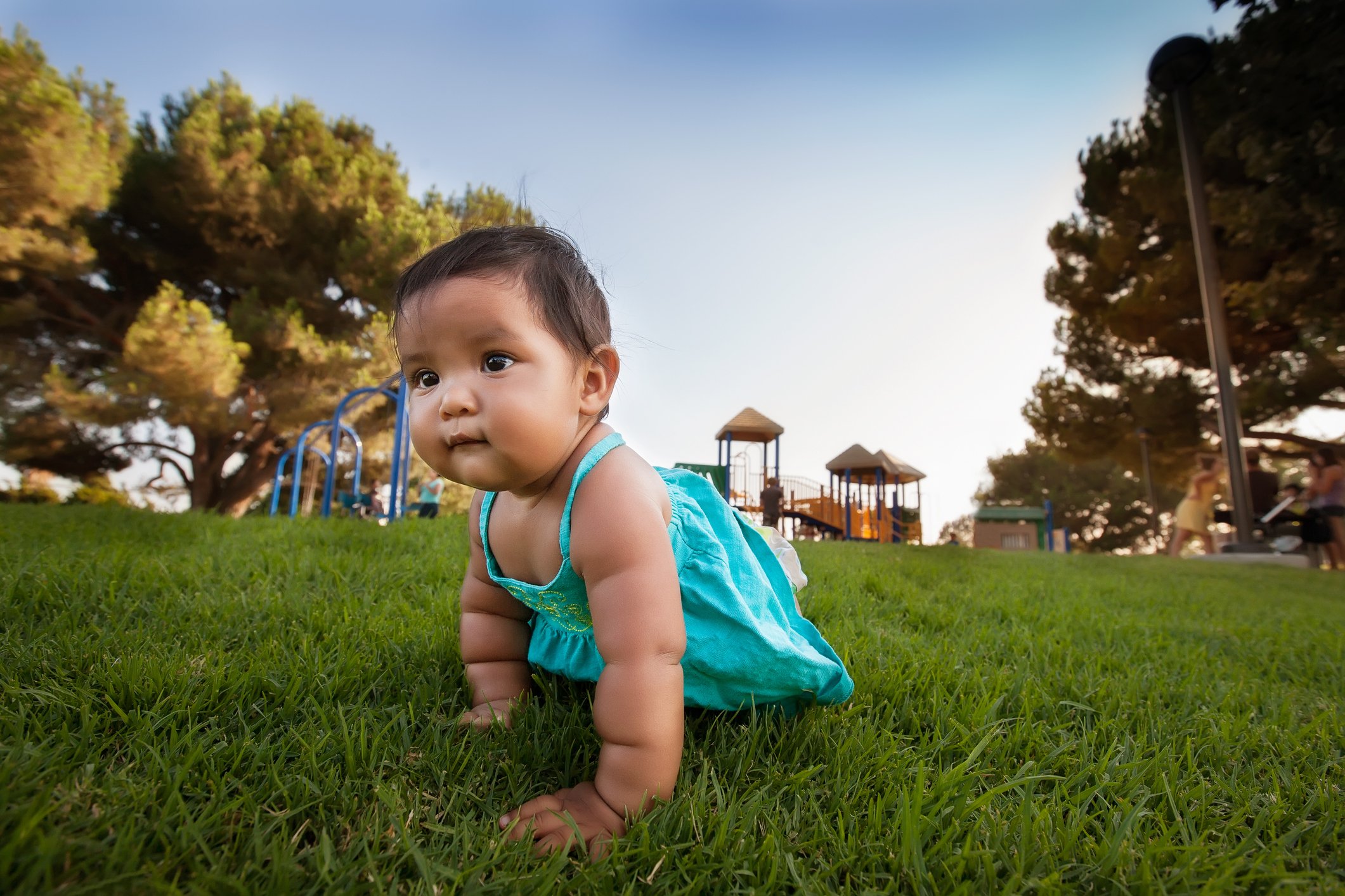 A curious little baby girl crawls away from a kids playground to explore, and is unsupervised by parents.