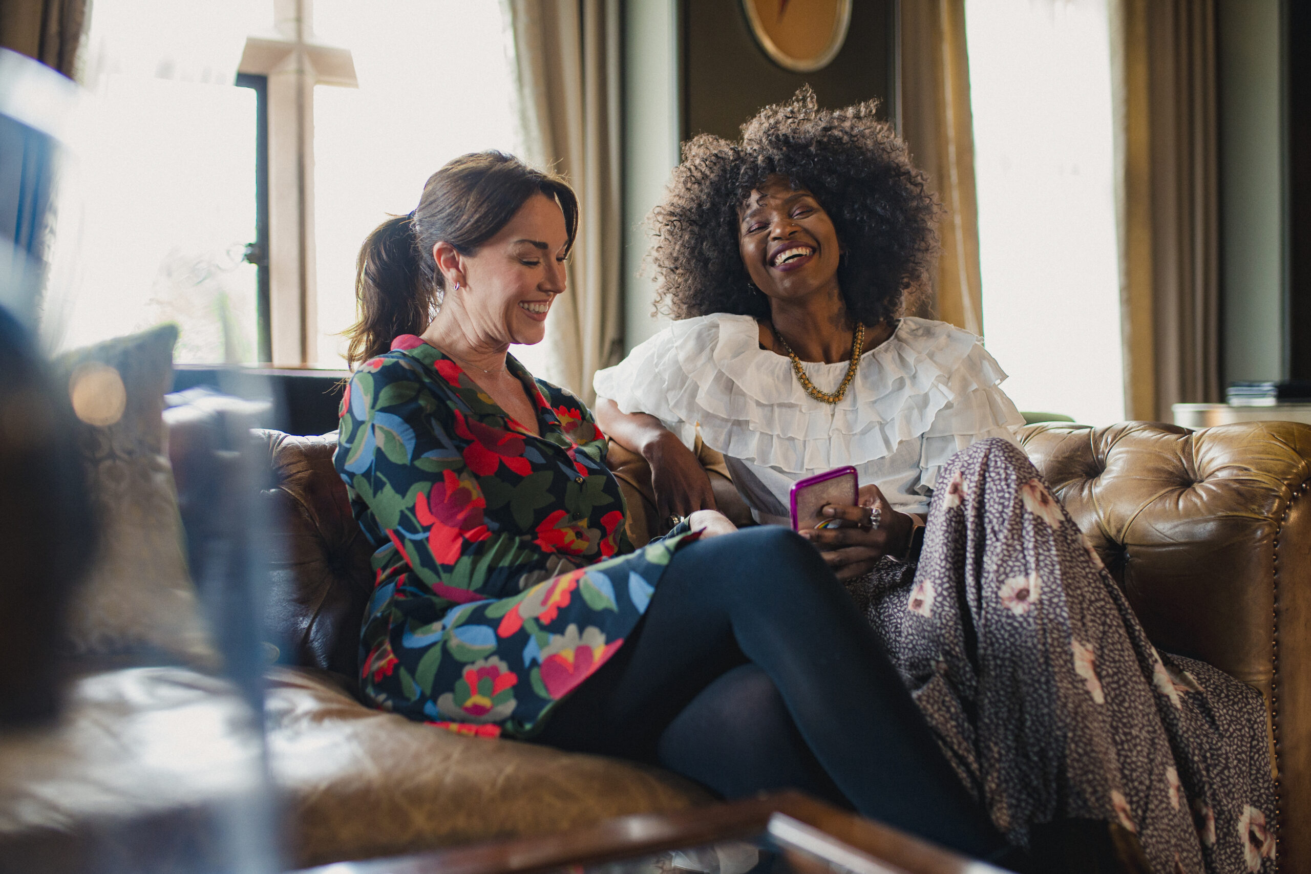 two women talking and laughing on the couch