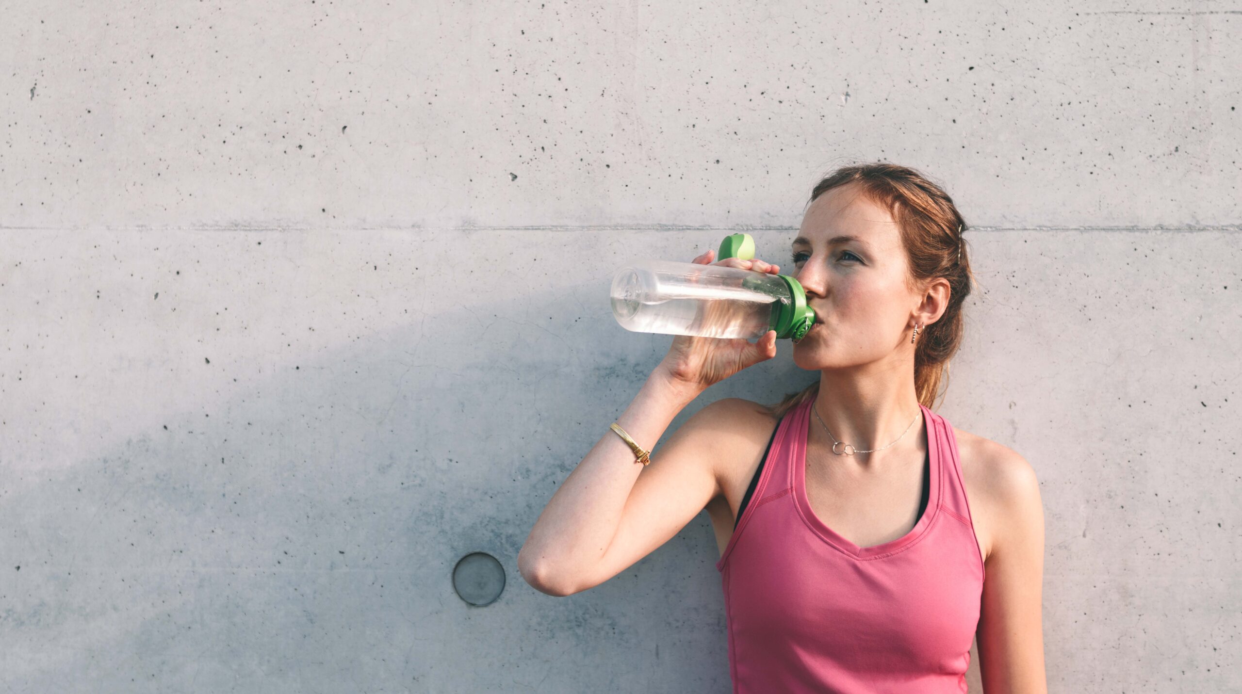 sportswoman drinking water in front of concrete wall