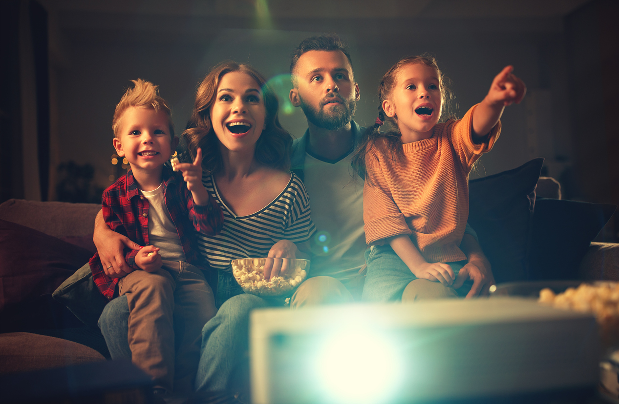 family mother father and children watching projector, TV, movies with popcorn in evening at home