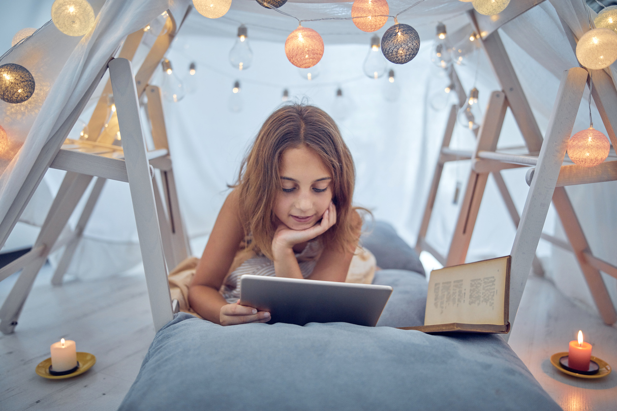 Little 10 year old girl using tablet under her home-made tent inside the living room.