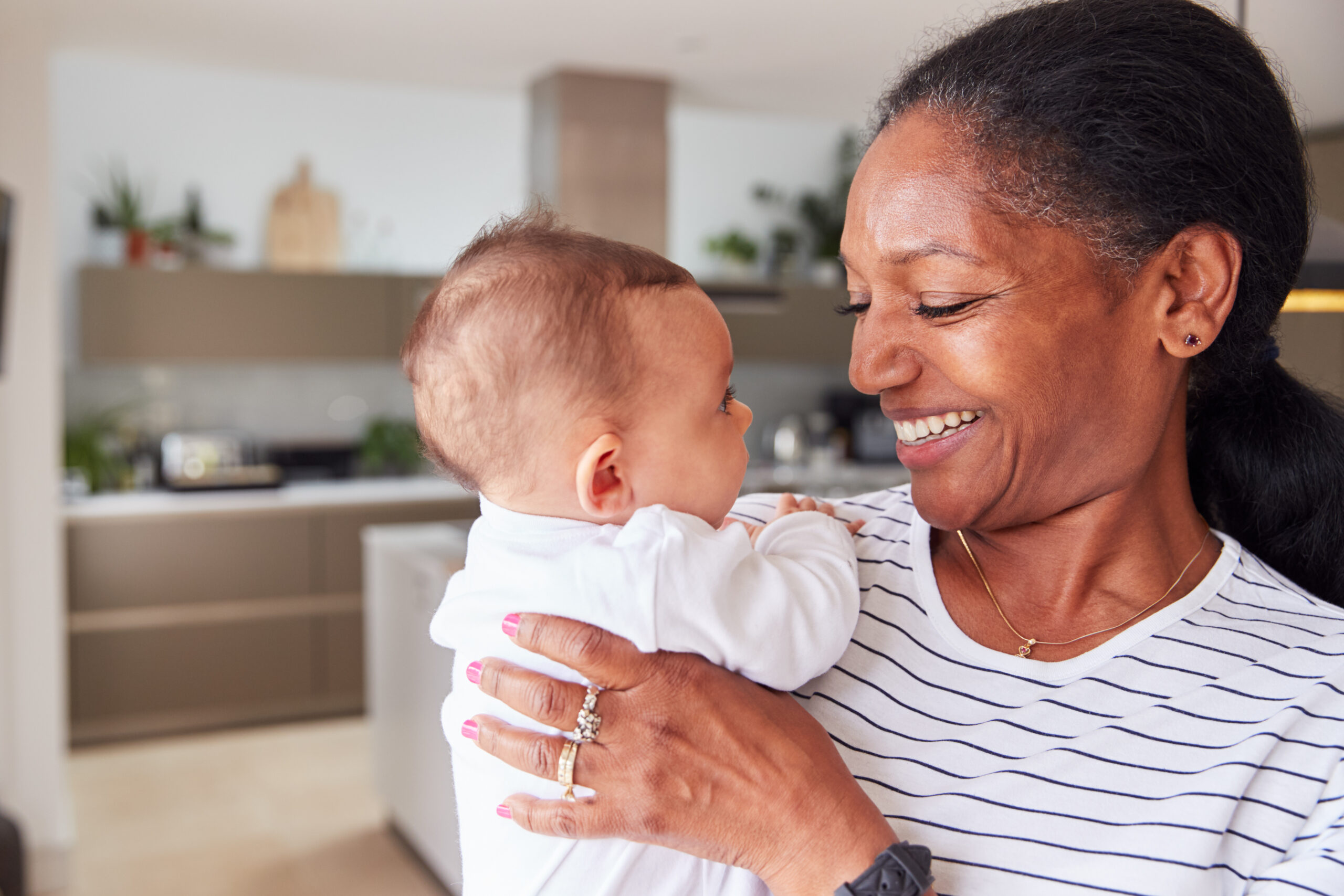 Loving Grandmother Holding 3 Month Old Baby Granddaughter In Kitchen At Home