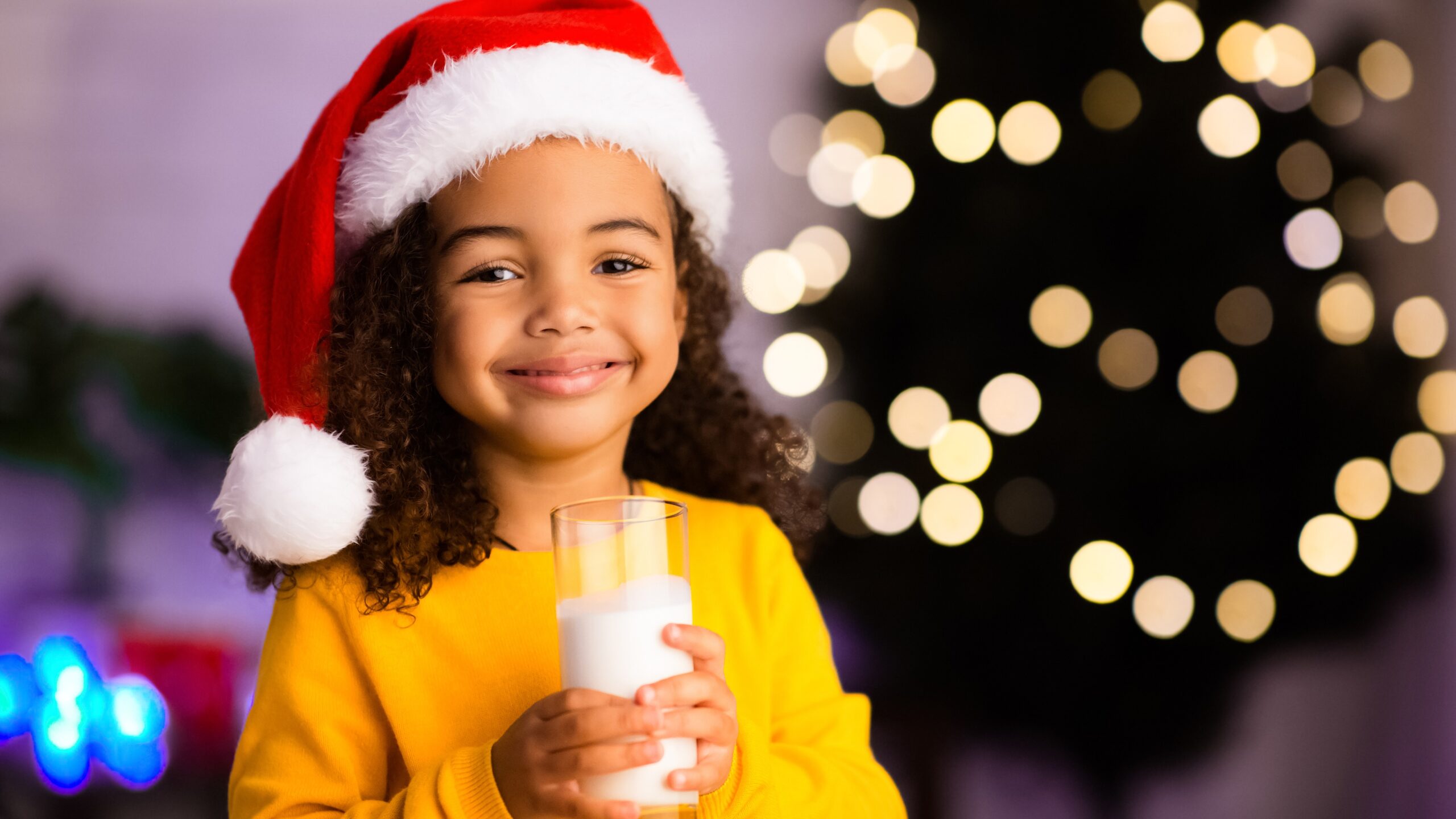 young girl wearing Chrsitmas hat holding a glass of milk