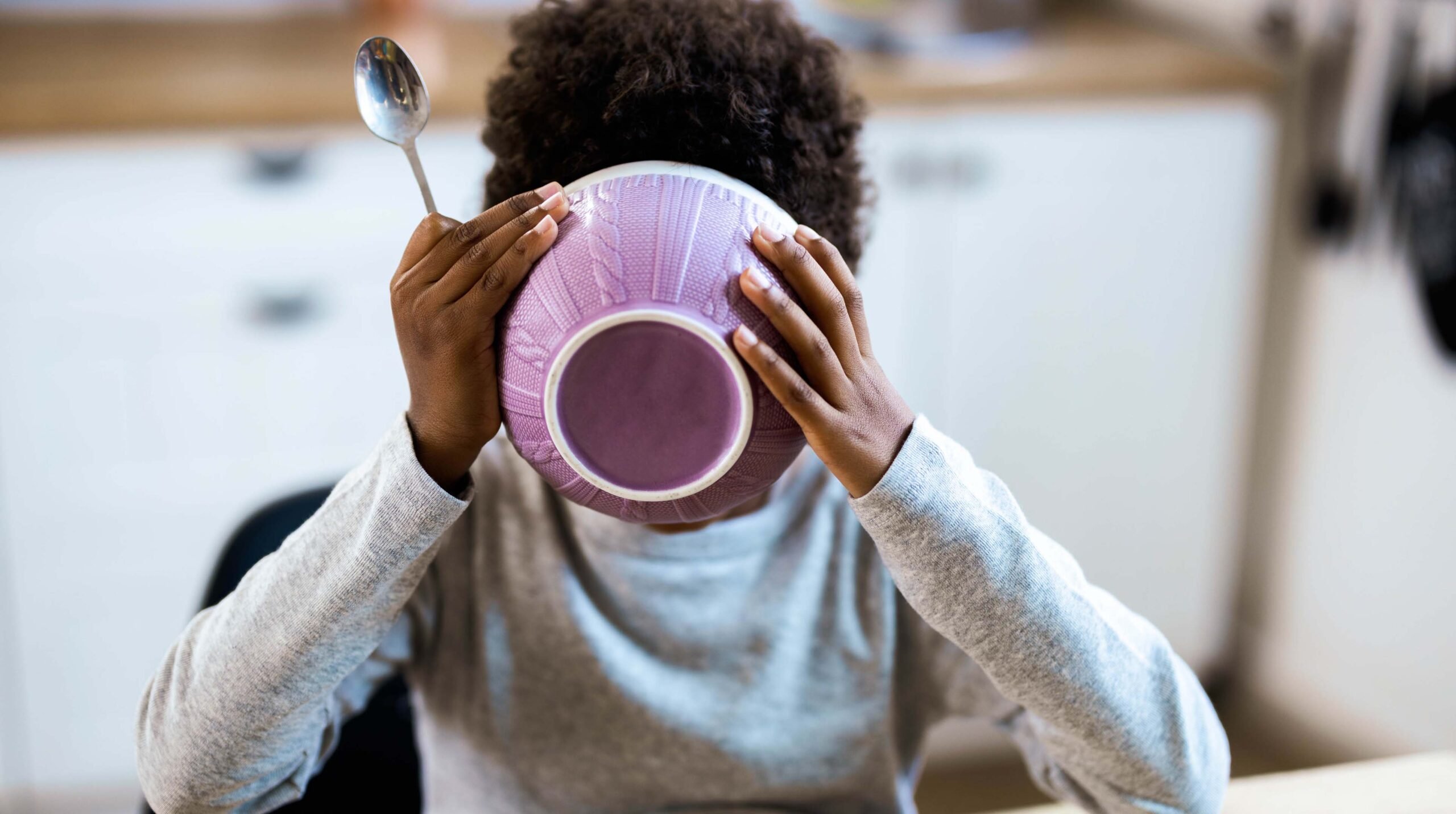 Small black kid eating his breakfast from a bowl at dining table.