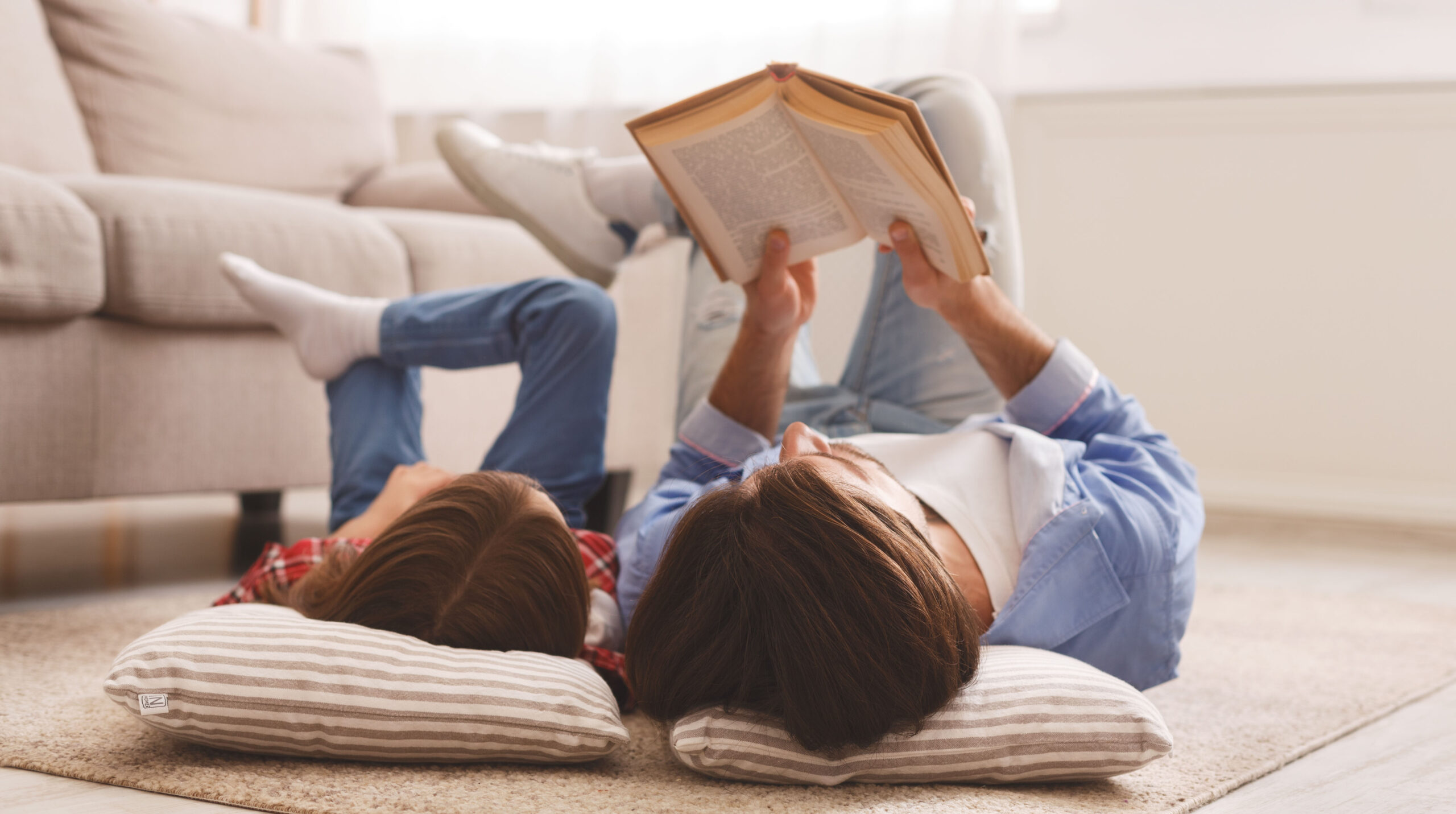 Little girl and father enjoying book together, laying on floor