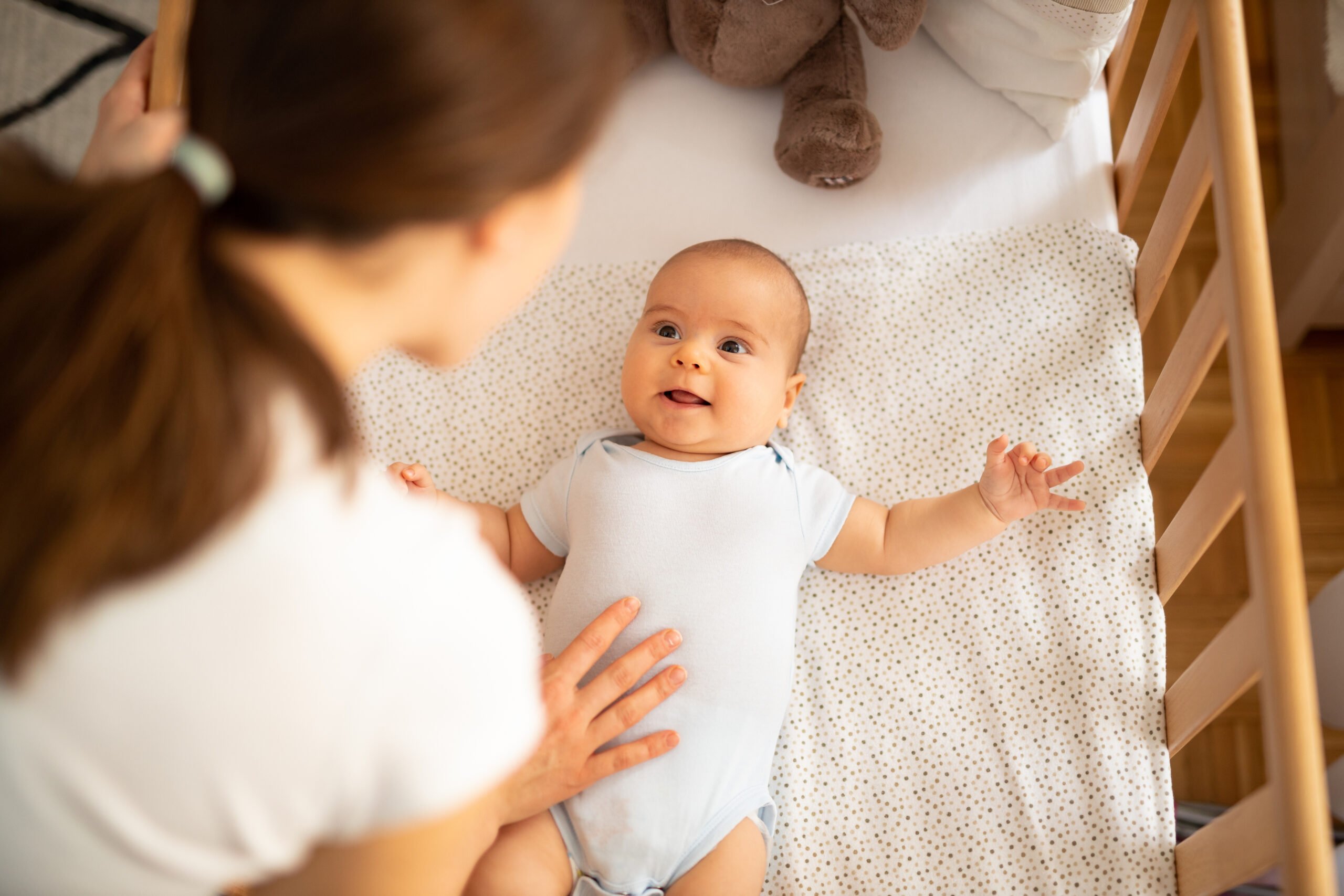 Mother putting her baby to sleep. Woman bending forward over a crib to check her baby.