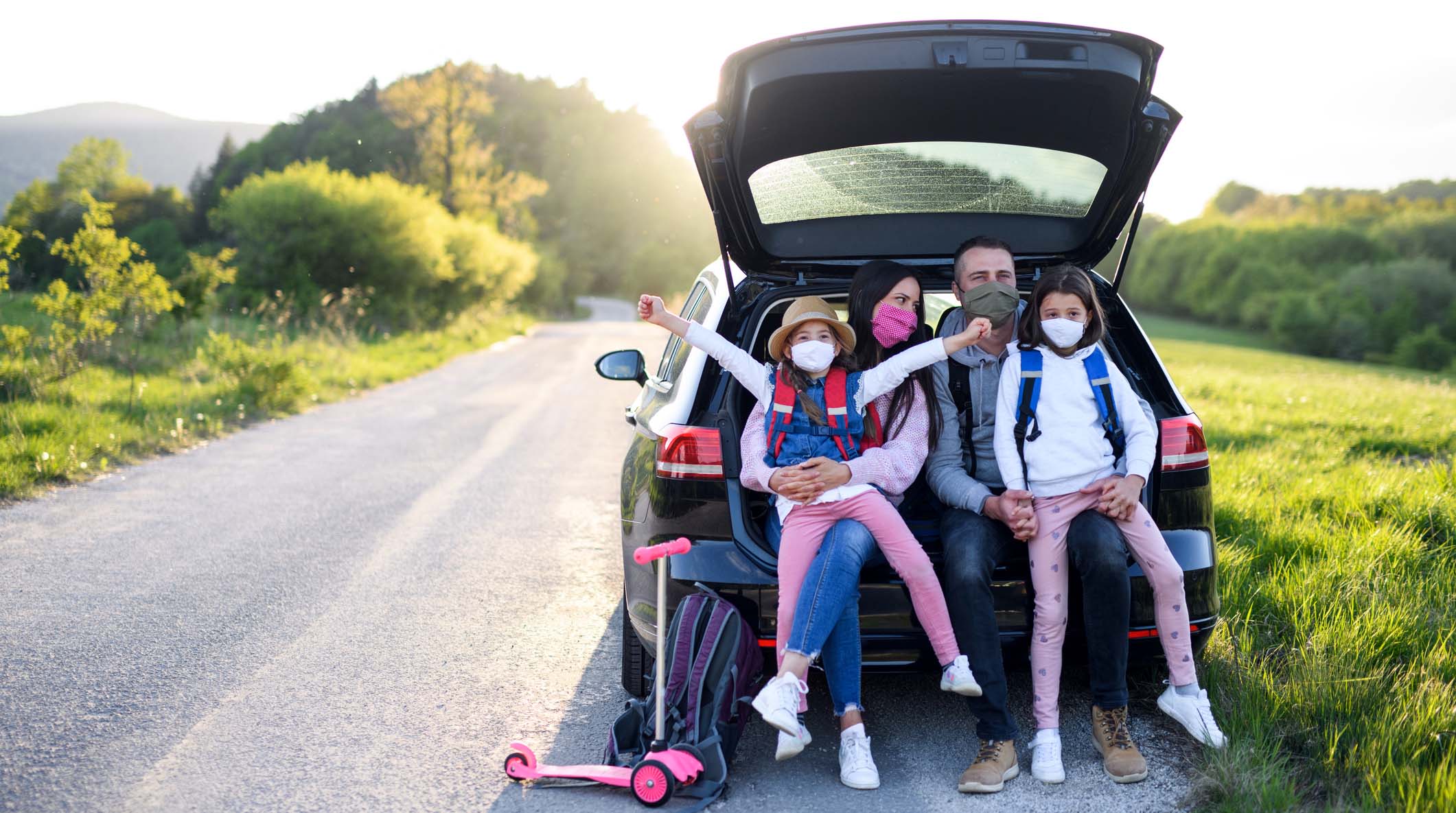 Family with two small daughters on trip outdoors in nature, wearing face masks.