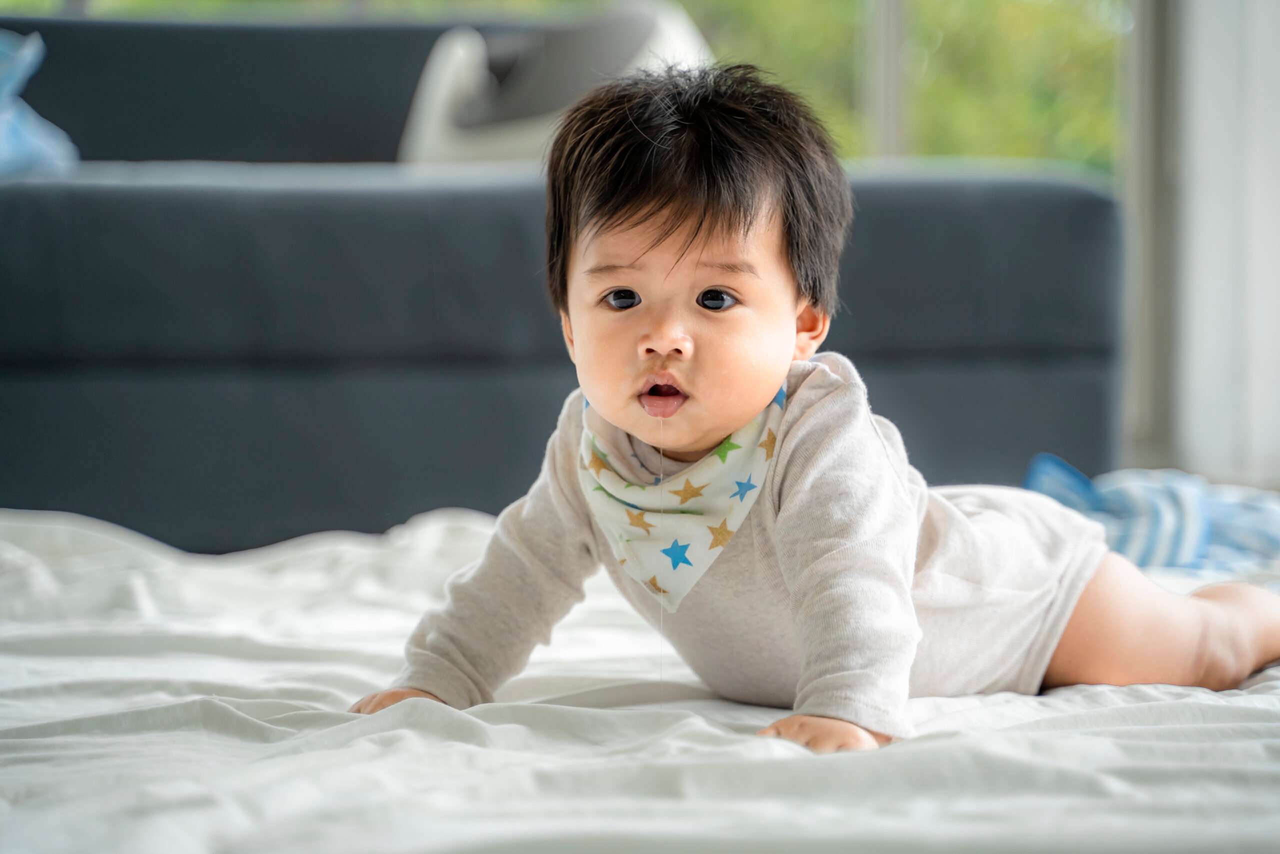 An Asian baby is crawling along the floor on a room covered by a quilt.