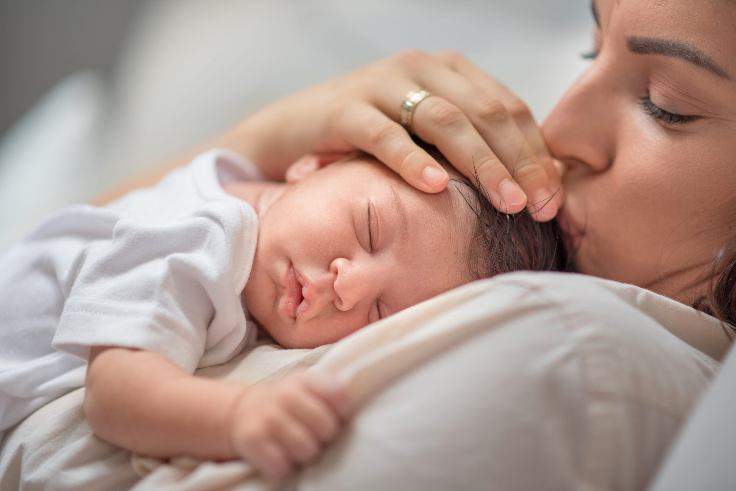 Mother kissing newborn baby boy head while putting her child to sleep