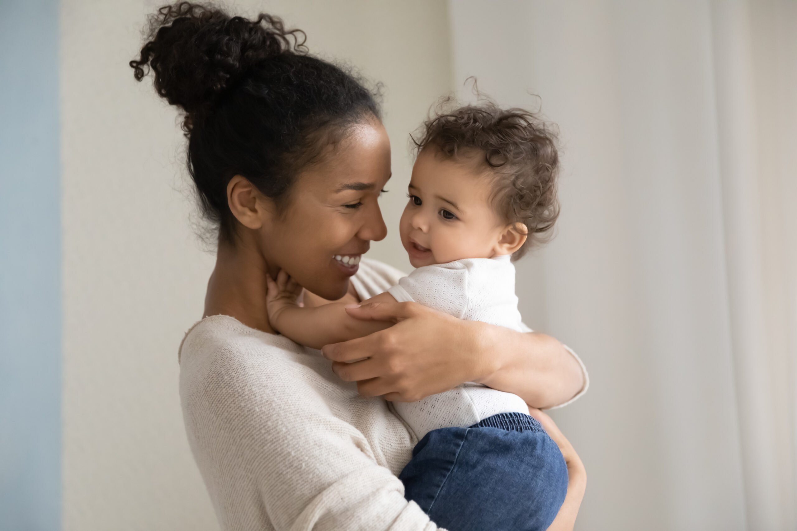 Affectionate millennial biracial mom carrying on hands funny kid.