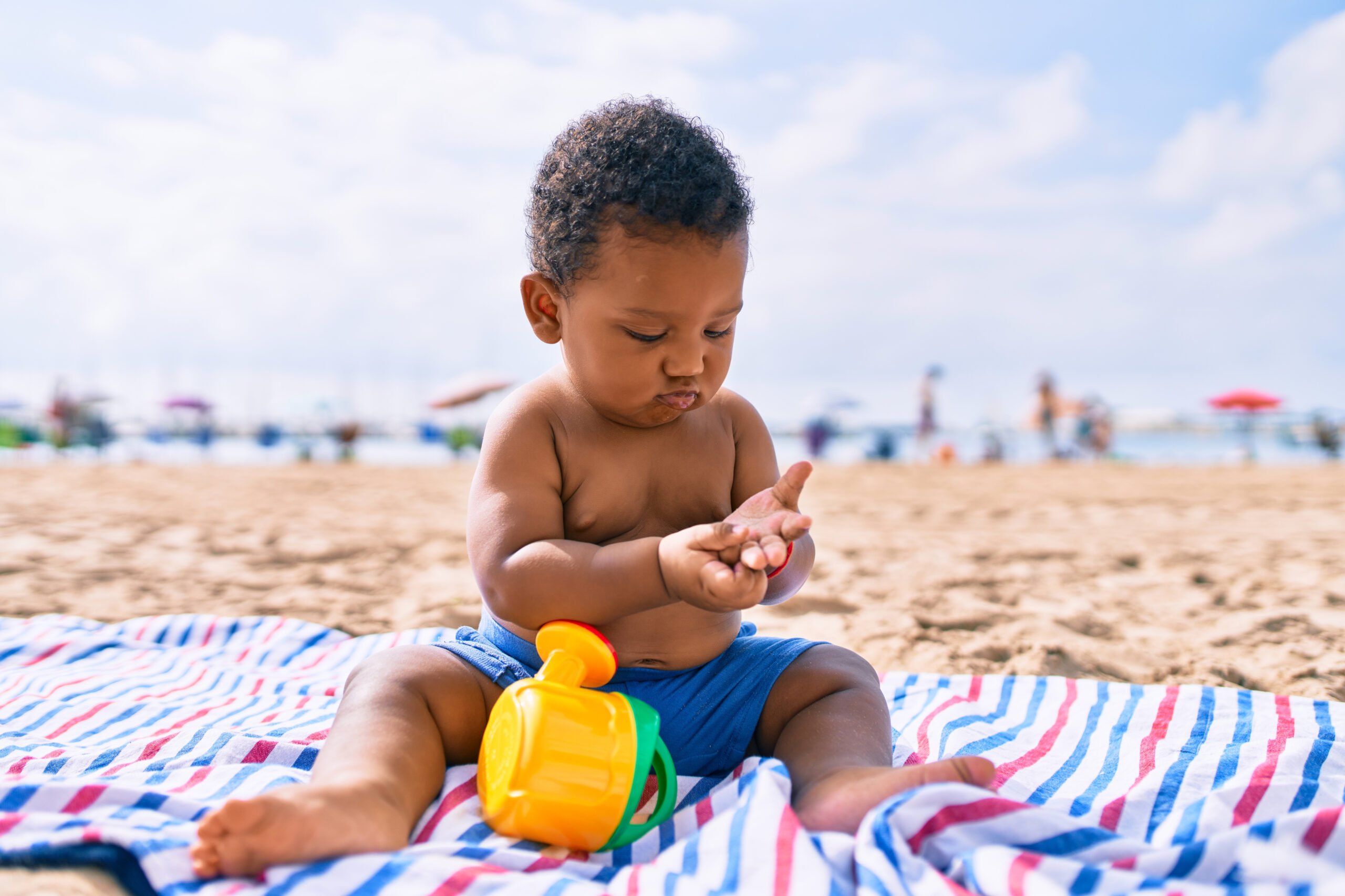 Adorable african american toddler playing with toys sitting on the sand at the beach.