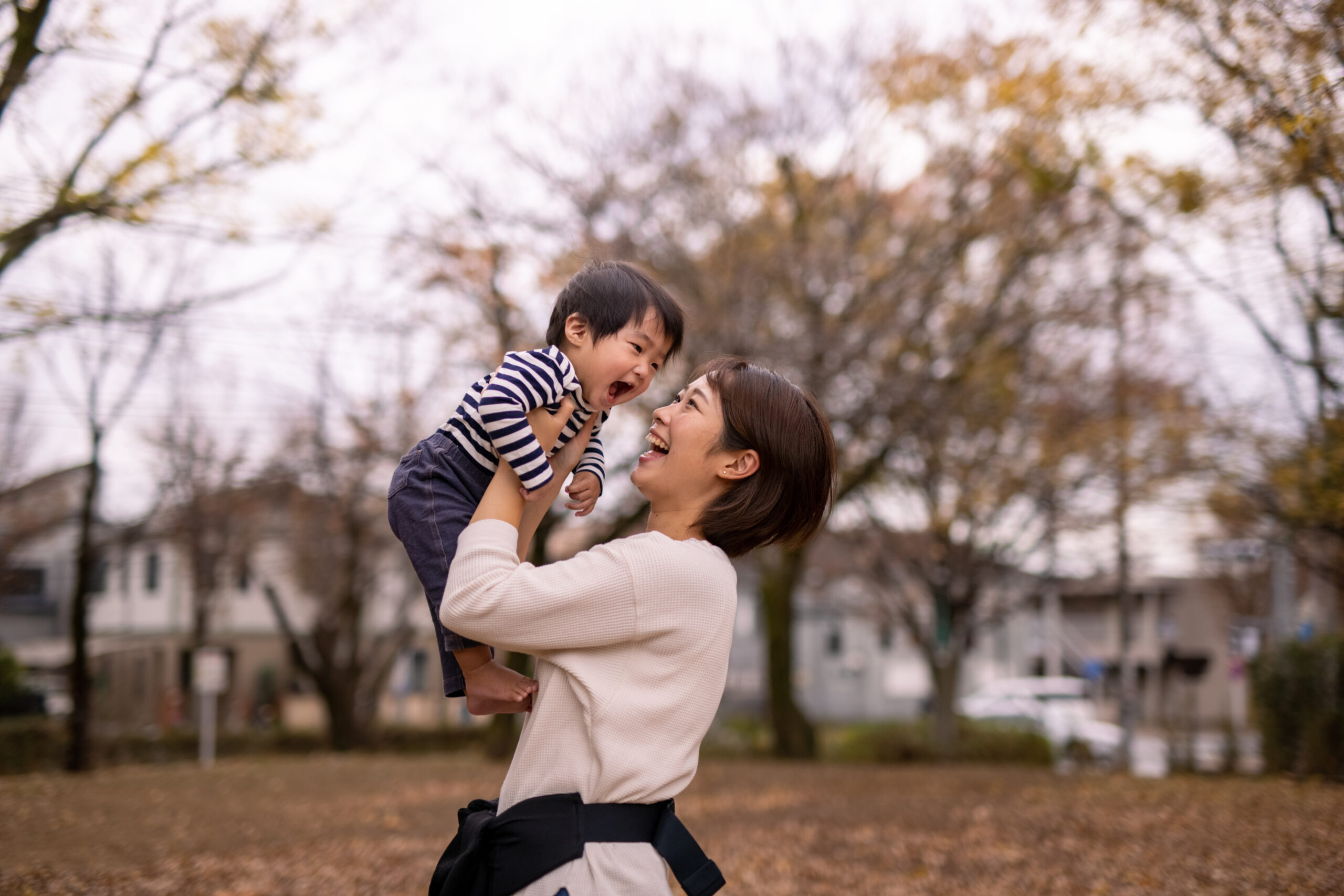 Young mother lifting her son up in public park in autumn