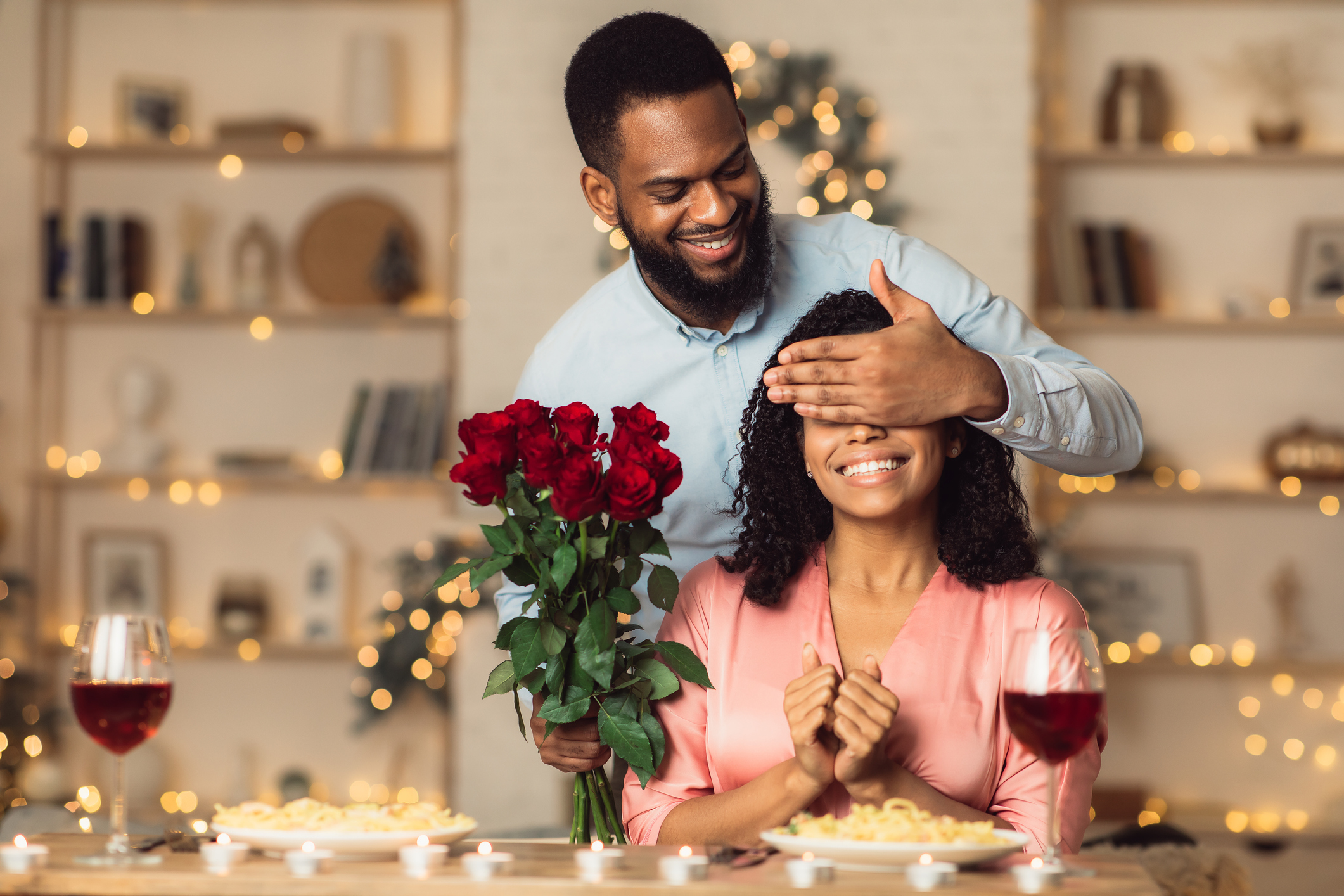 Young black man giving flowers to woman, covering eyes
