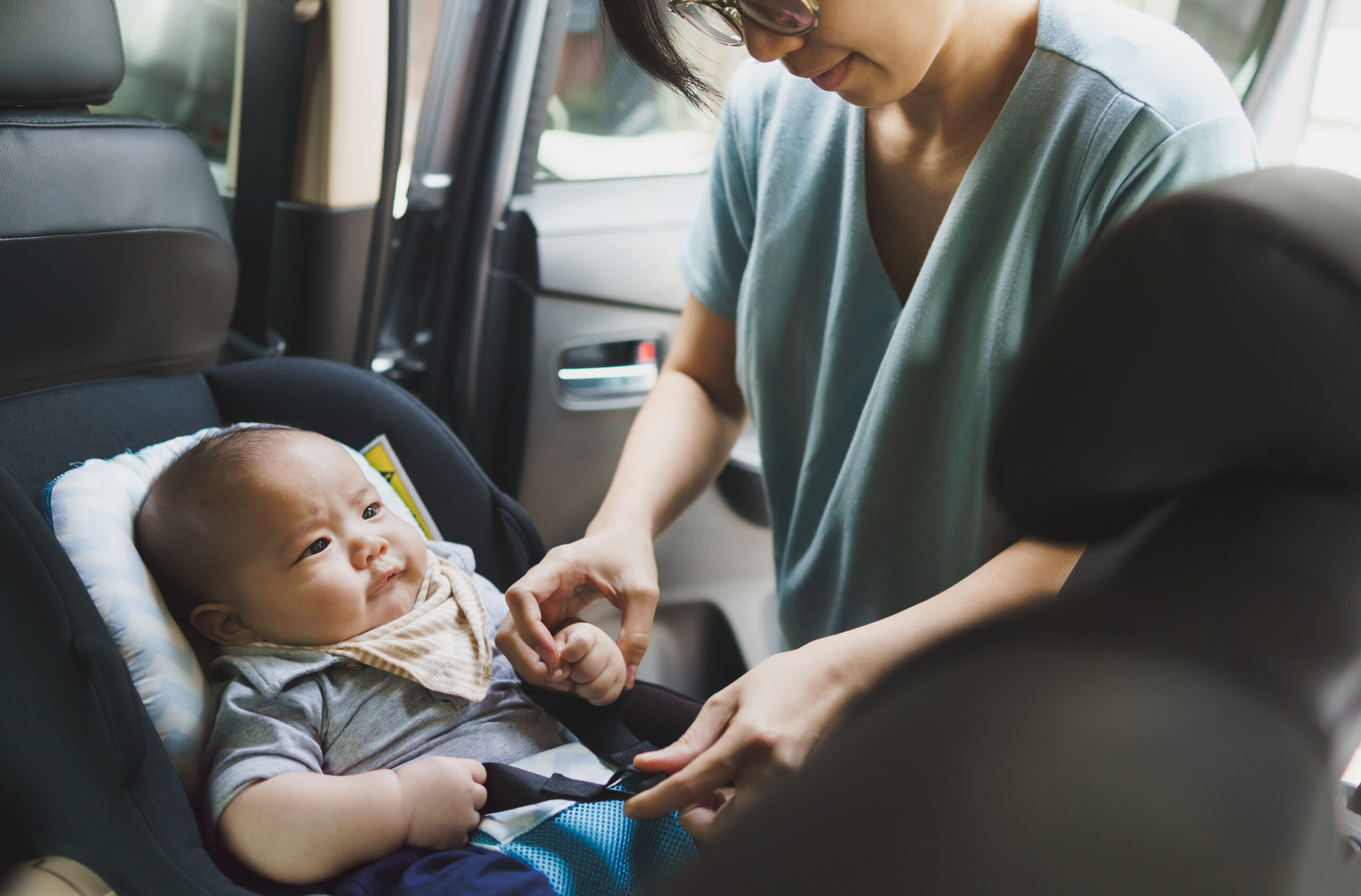 Asian Mother helping her little baby boy son to fasten belt on his car seat in car