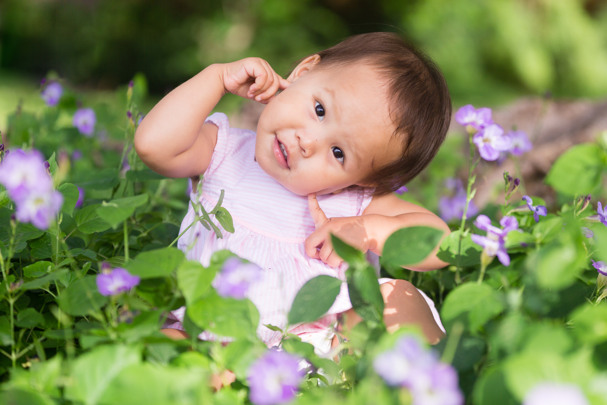 Cute pretty portrait of playful happy baby girl in the flower garden.