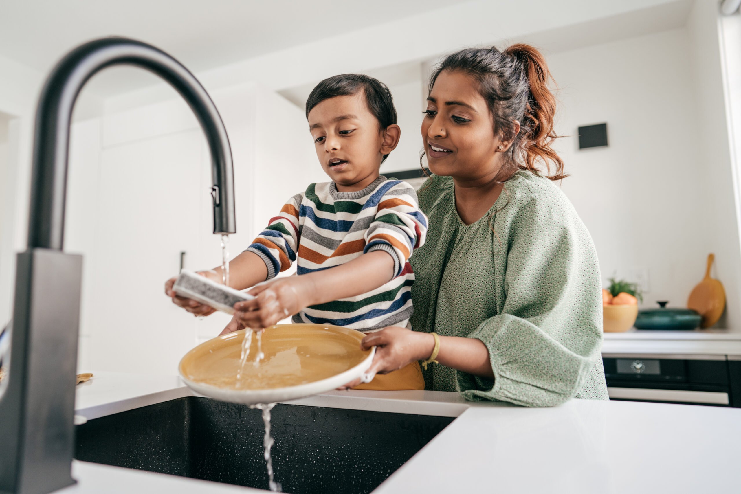 mom teaching son to wash dishes