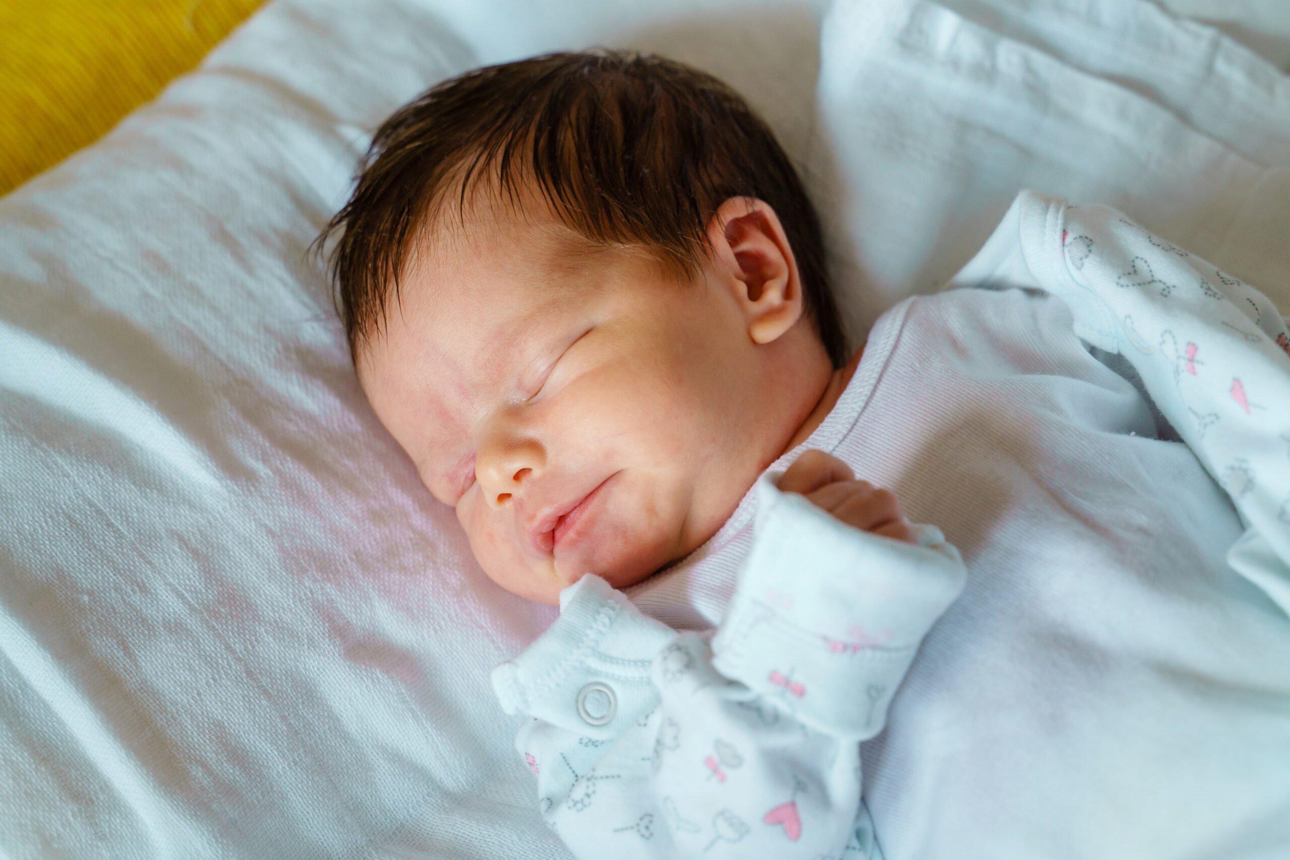 Close up on newborn happy caucasian baby sleeping in bed at home on first day of her life - cute little infant girl sleep peacefully