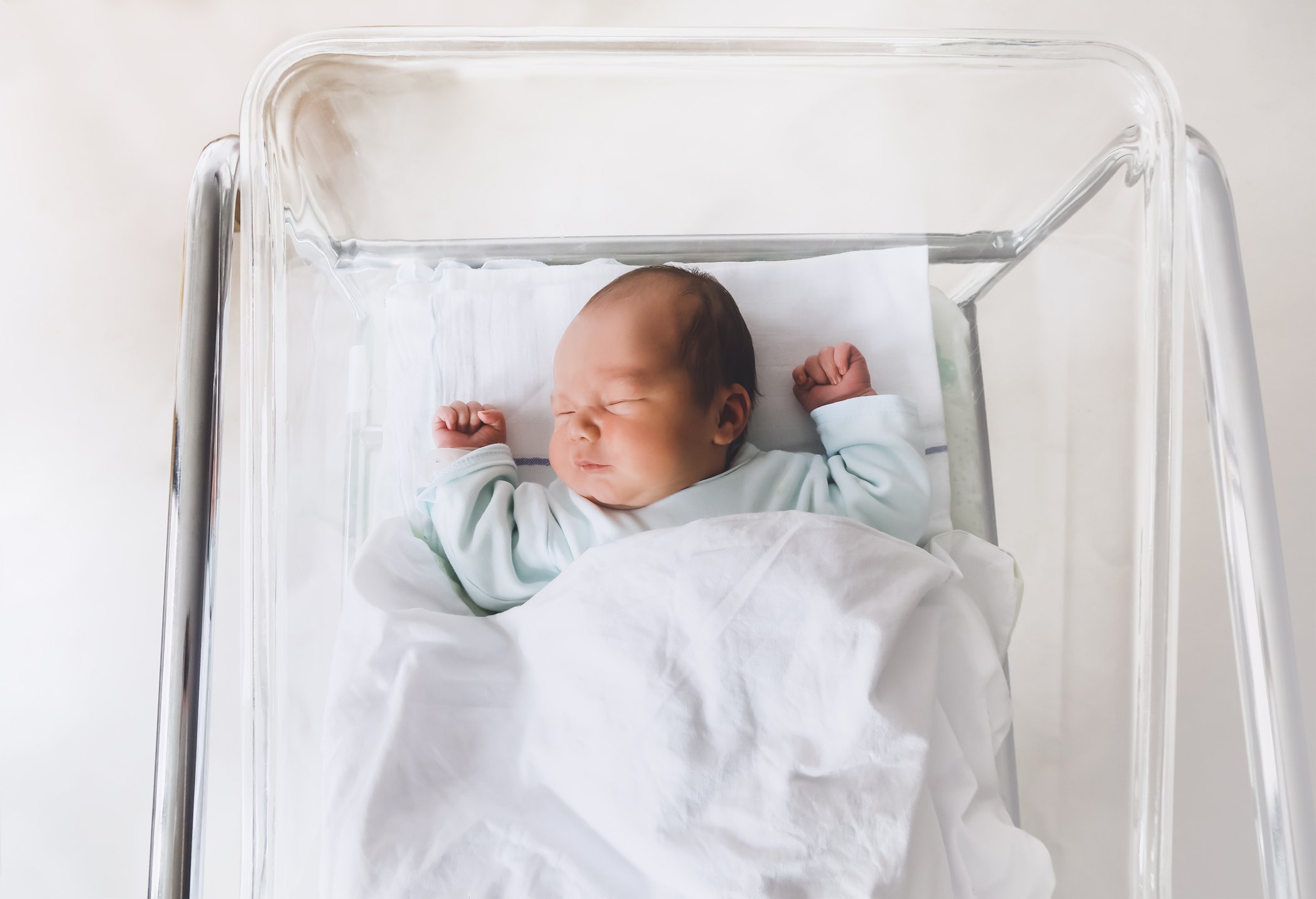 Newborn baby is sleeping in small transparent portable plastic bed.