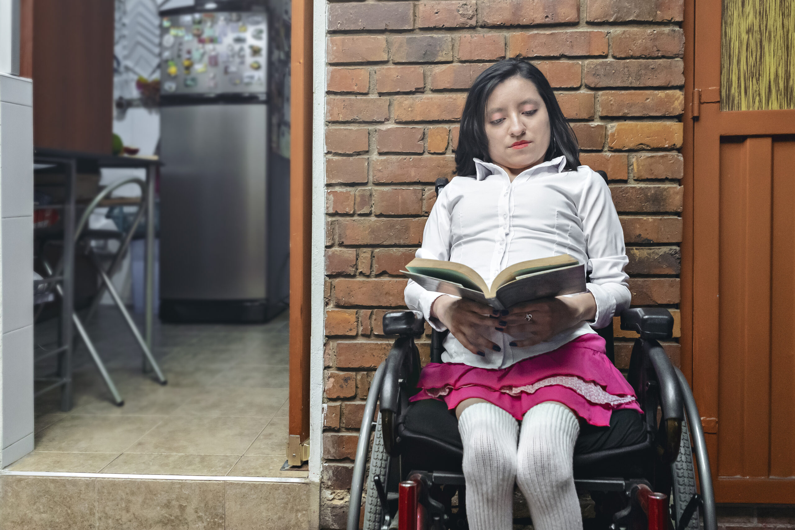 Disabled woman reading a book in a wheelchair in her backyard