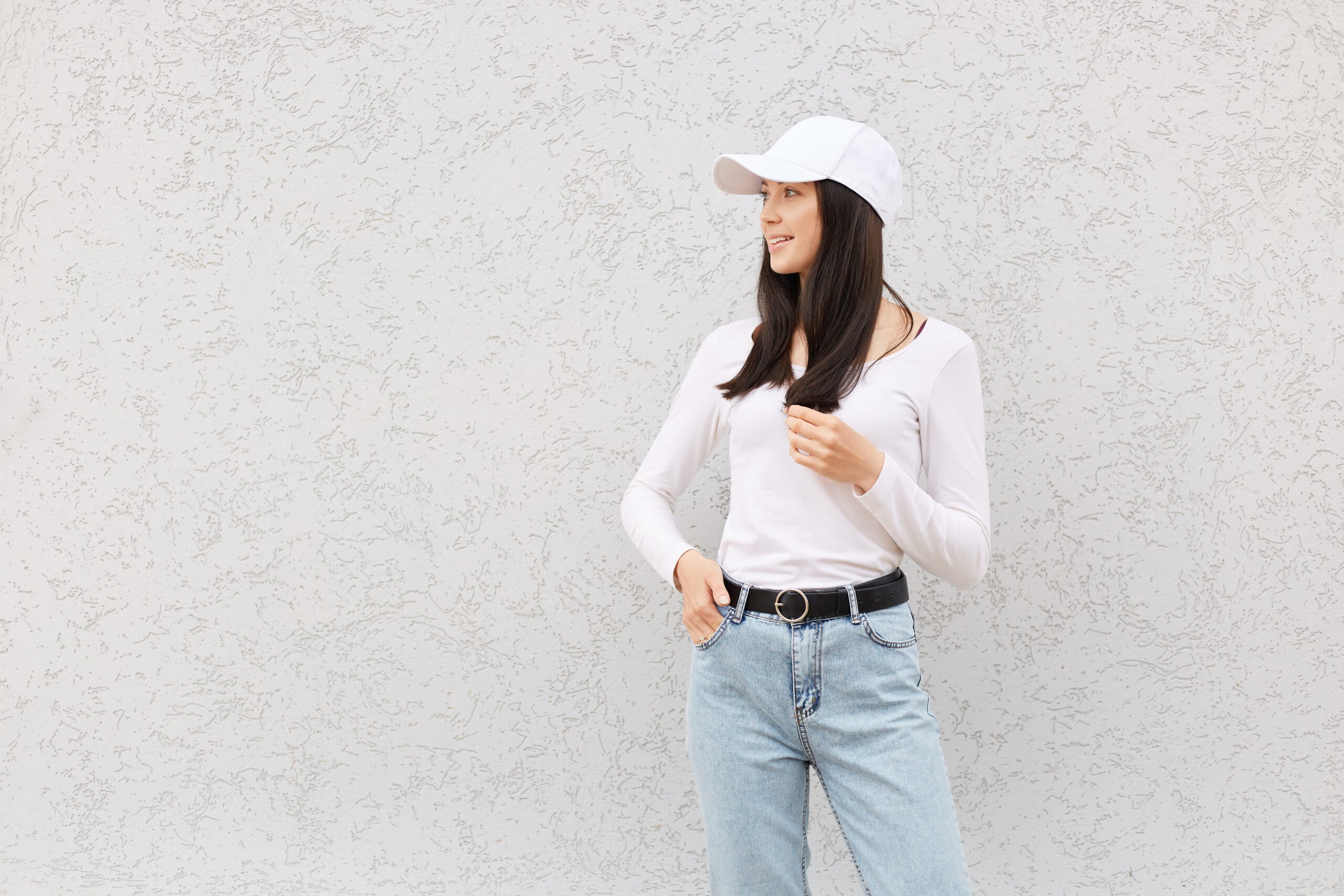 Beautiful European female wearing white shirt, jeans and baseball cap, woman with pleasant appearance looking away, expressing positive emotions, copy space for promotional text.
