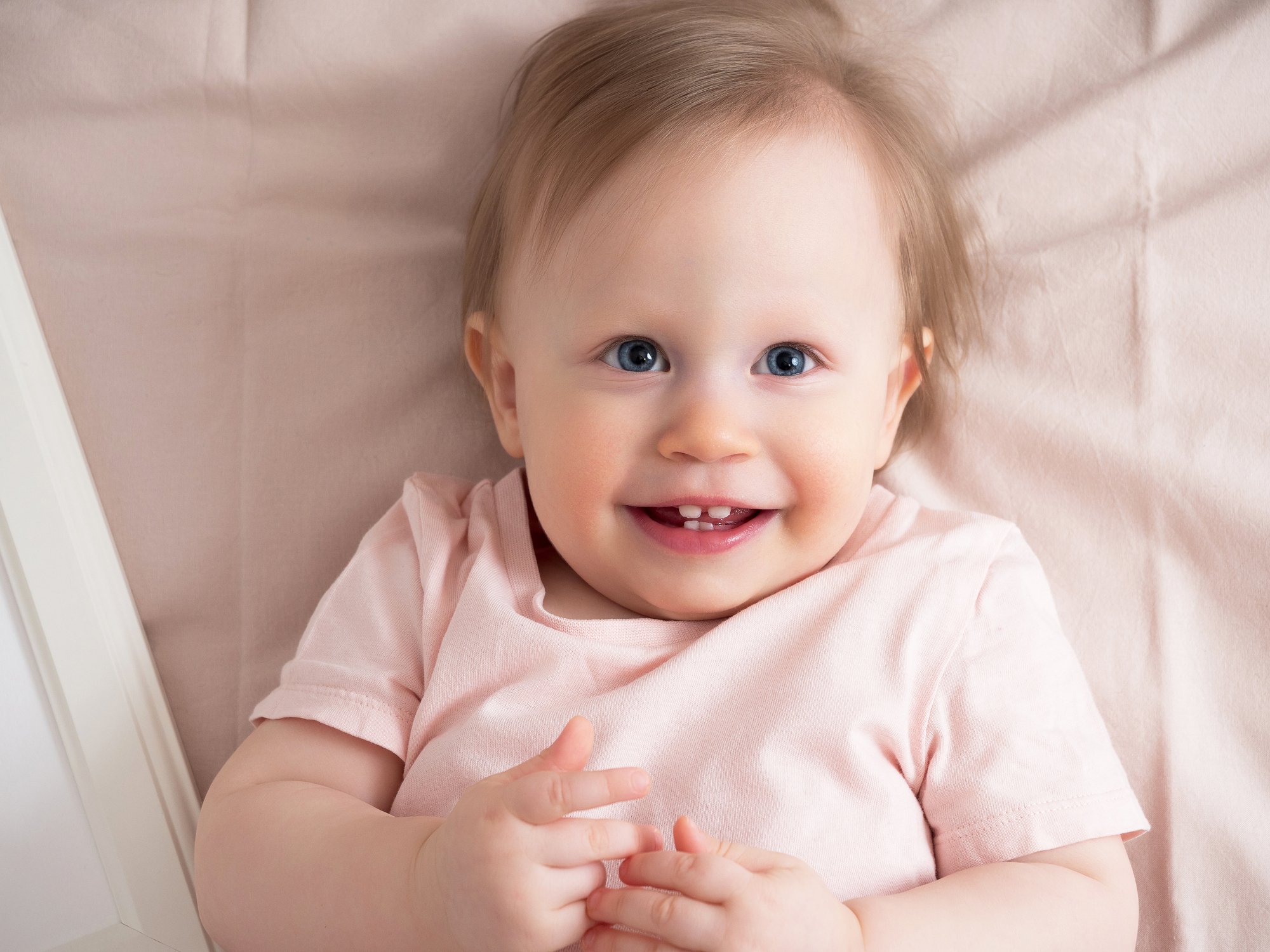 Portrait of a happy laughing baby, with a funny expression on his face. A small beautiful girl with blue eyes smiles cheerfully, the first teeth are visible