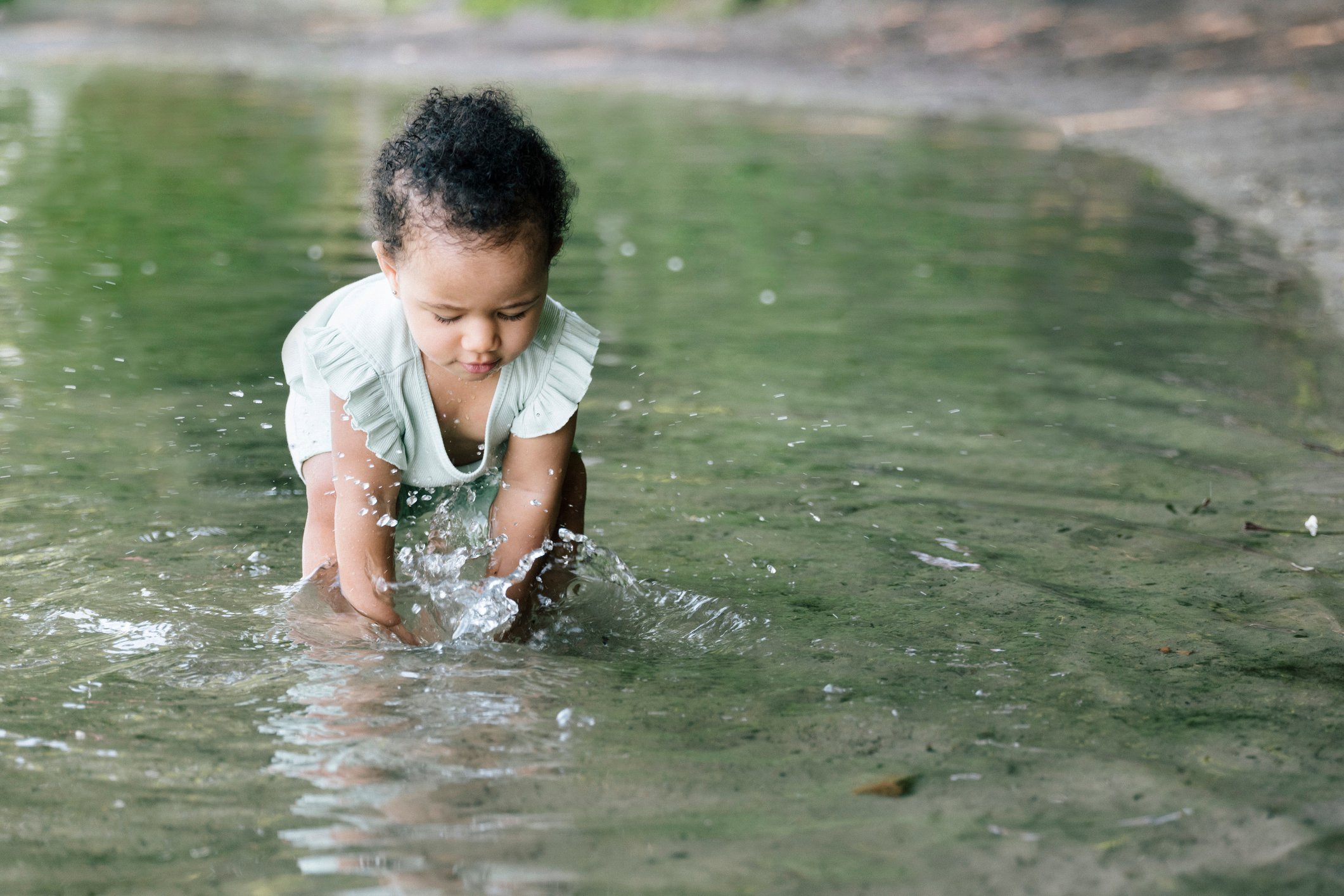 carefree summer day: first steps of a happy baby girl and splashing in a lake