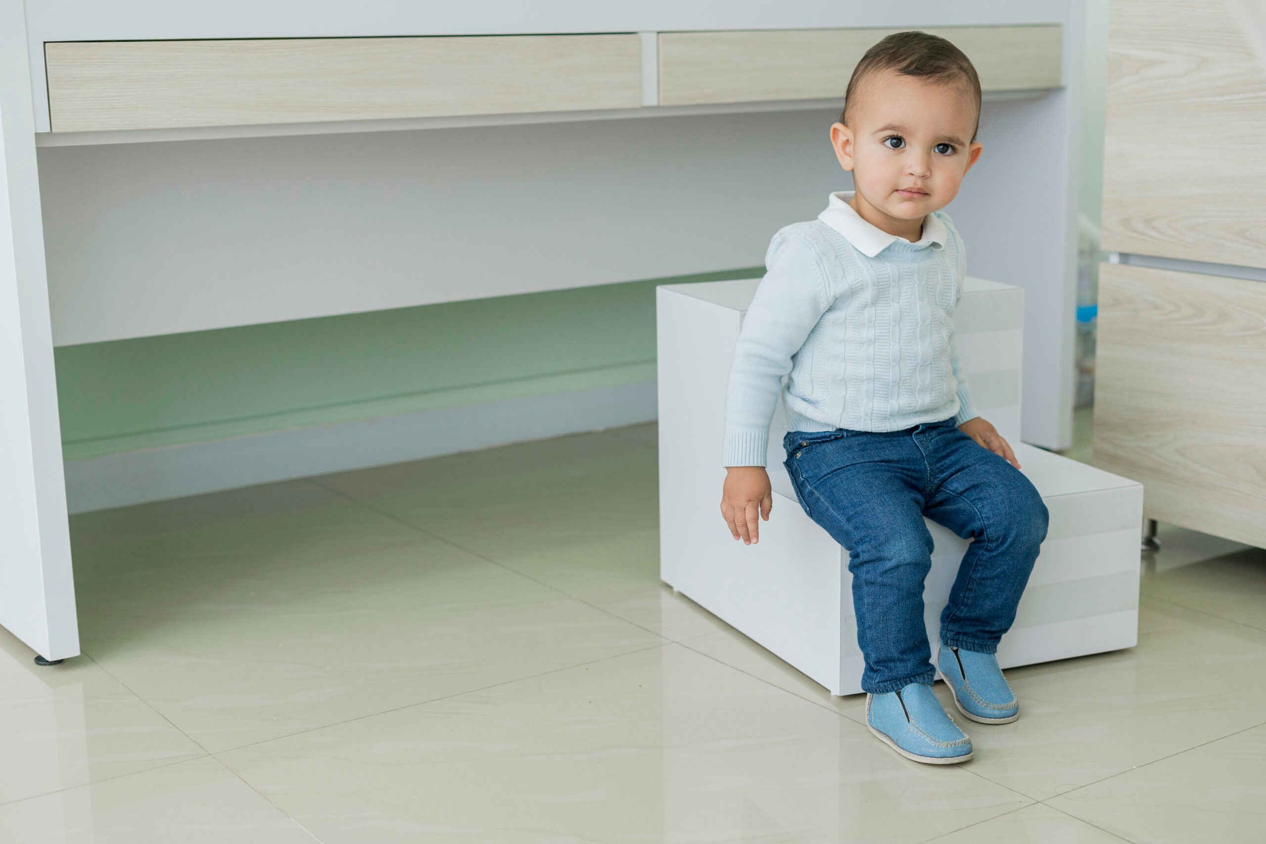 Portrait of a 2 year old boy looking at the camera when he arrives at the pediatrician's office for his periodic check-up while sitting on the stairs of the gurney looking at the camera before being treated