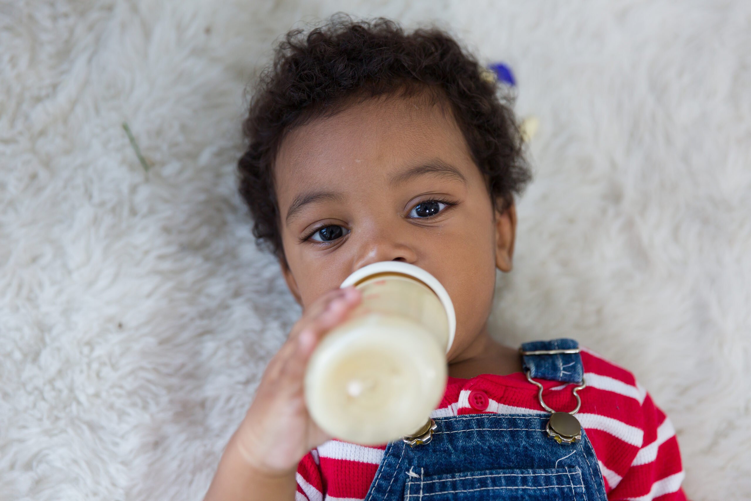 African American little boy lying on floor and eating milk from nipples