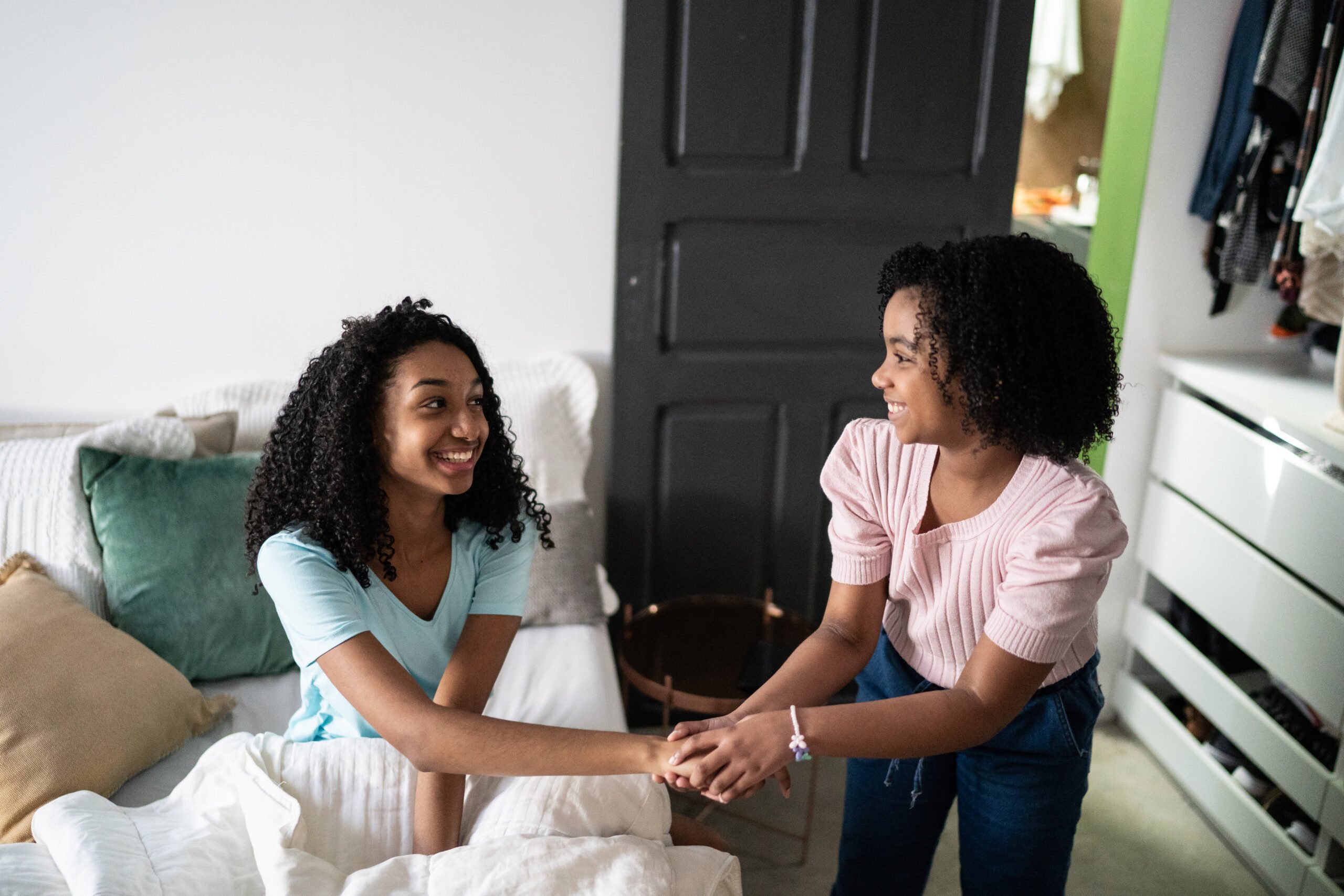 Girl waking up sister and holding her hands in the bedroom at home