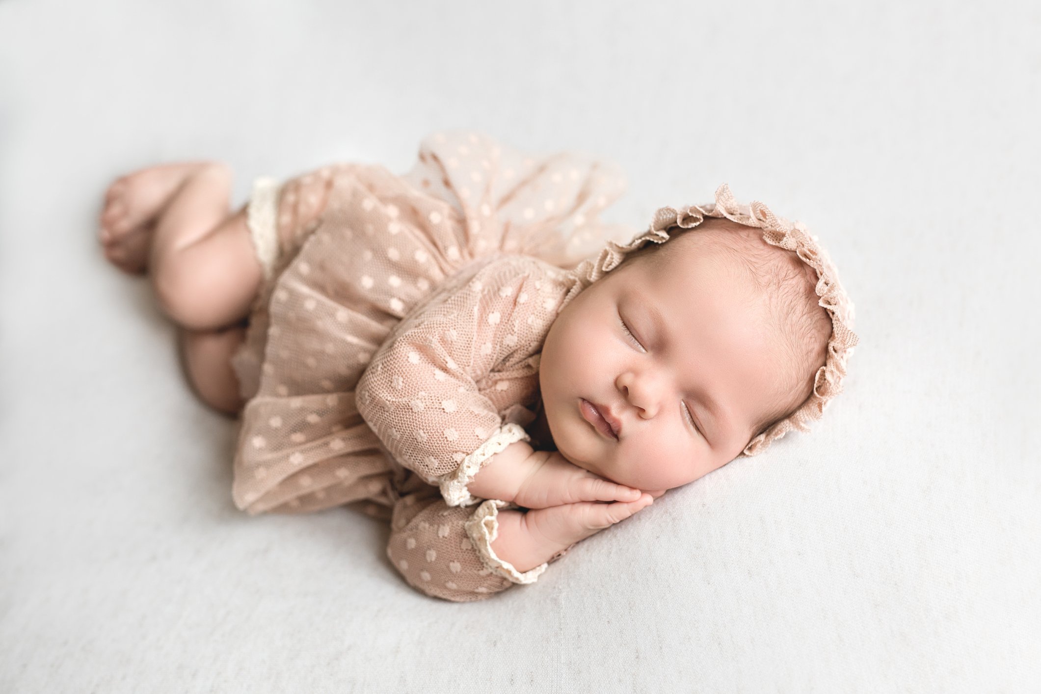The newborn sleeps sweetly with his hands tucked to his cheeks. Healthy baby sleep