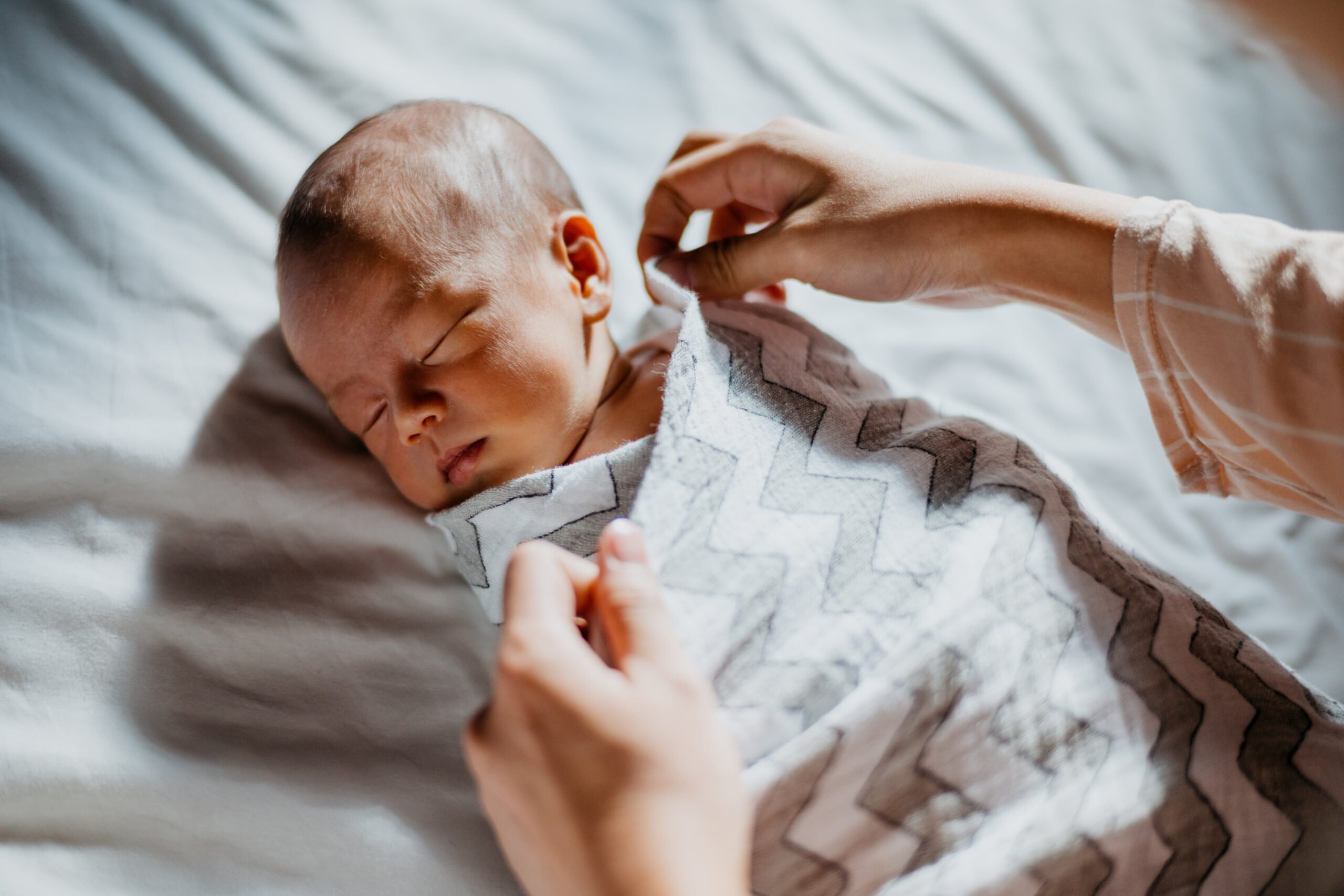 Mother swaddle her newborn baby on bed