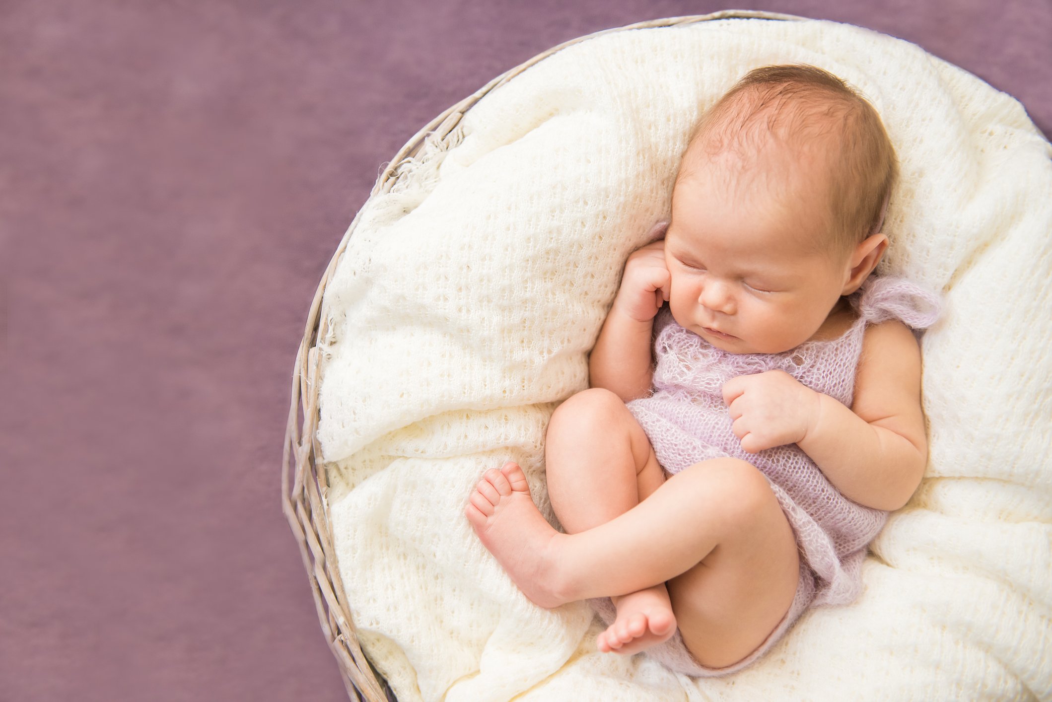 Newborn baby sleeping in round basket, purple background