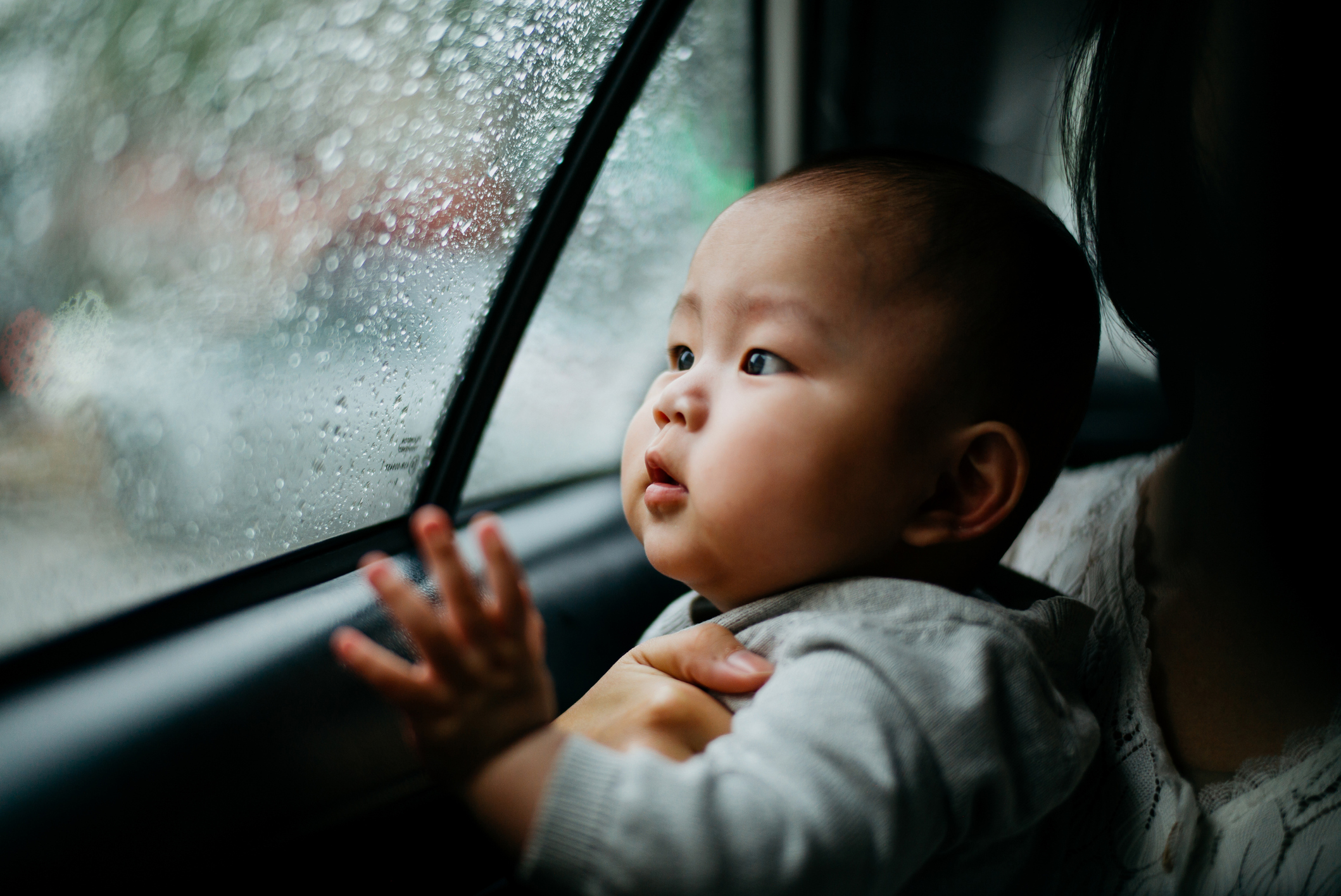 Asian baby boy looking out from car window on a rainy day