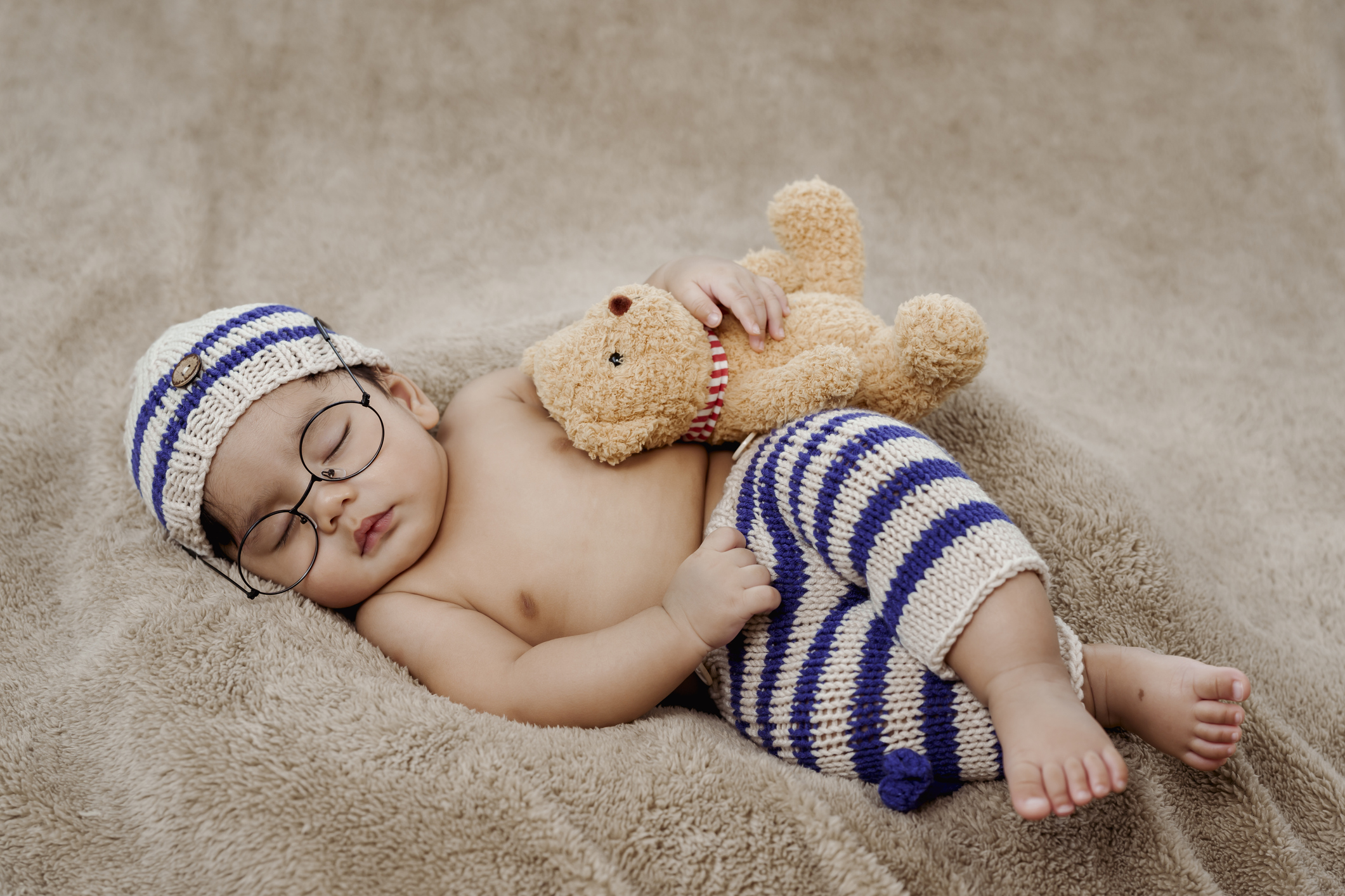 A 3-month-old Asian newborn in a knitted sweater is happily sleeping warmly on the rug in the bedroom. There was a brown teddy bear next to it. Concept Happy Family