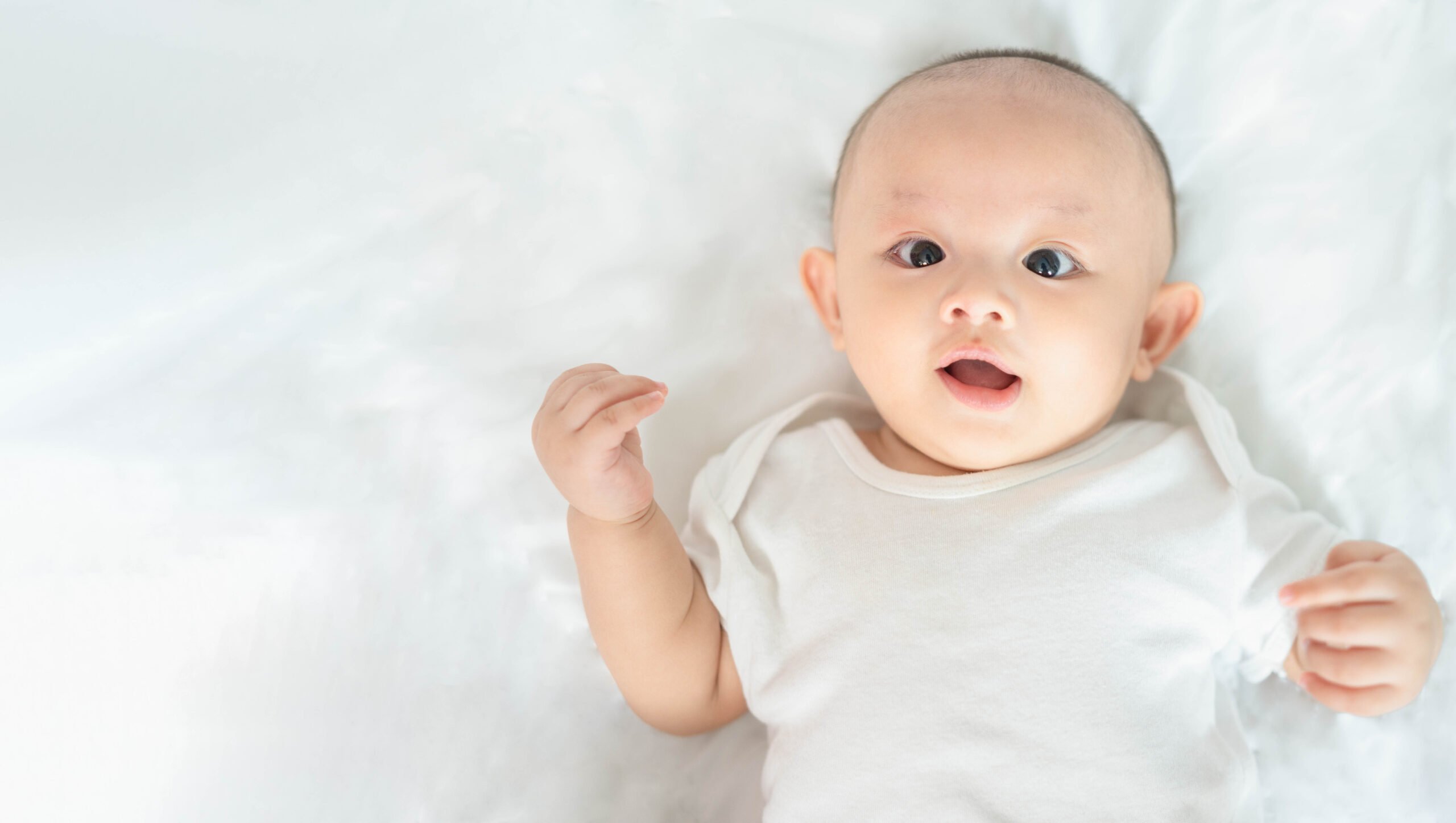 Happy family, Cute Asian newborn baby boy lying play on white bed look at camera with laughing smile happy face. Little innocent new infant adorable child in first day of life. Mother's Day concept.