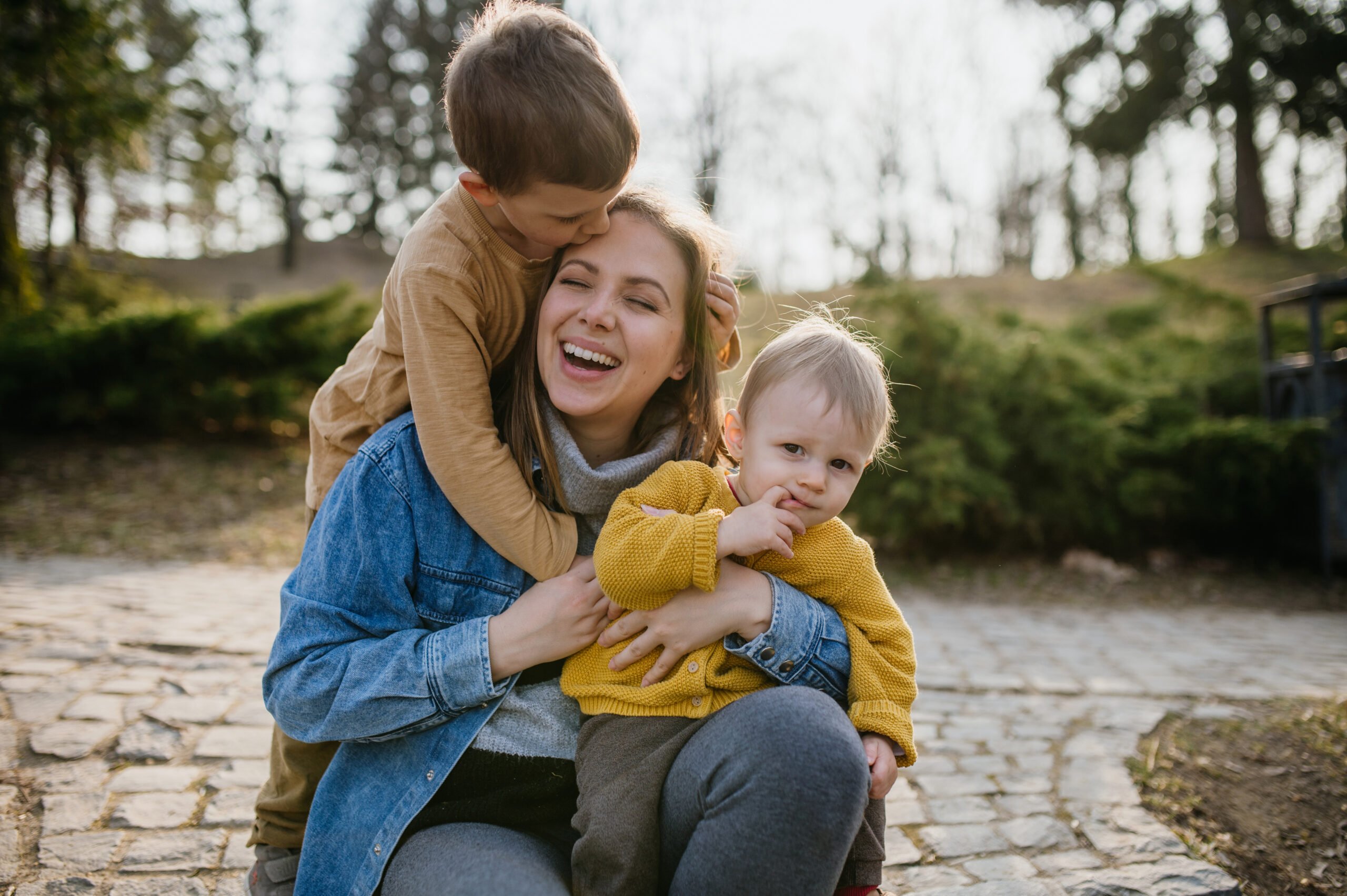 Happy young mother squatting and holding her little children, having fun, laughing in park in autumn.