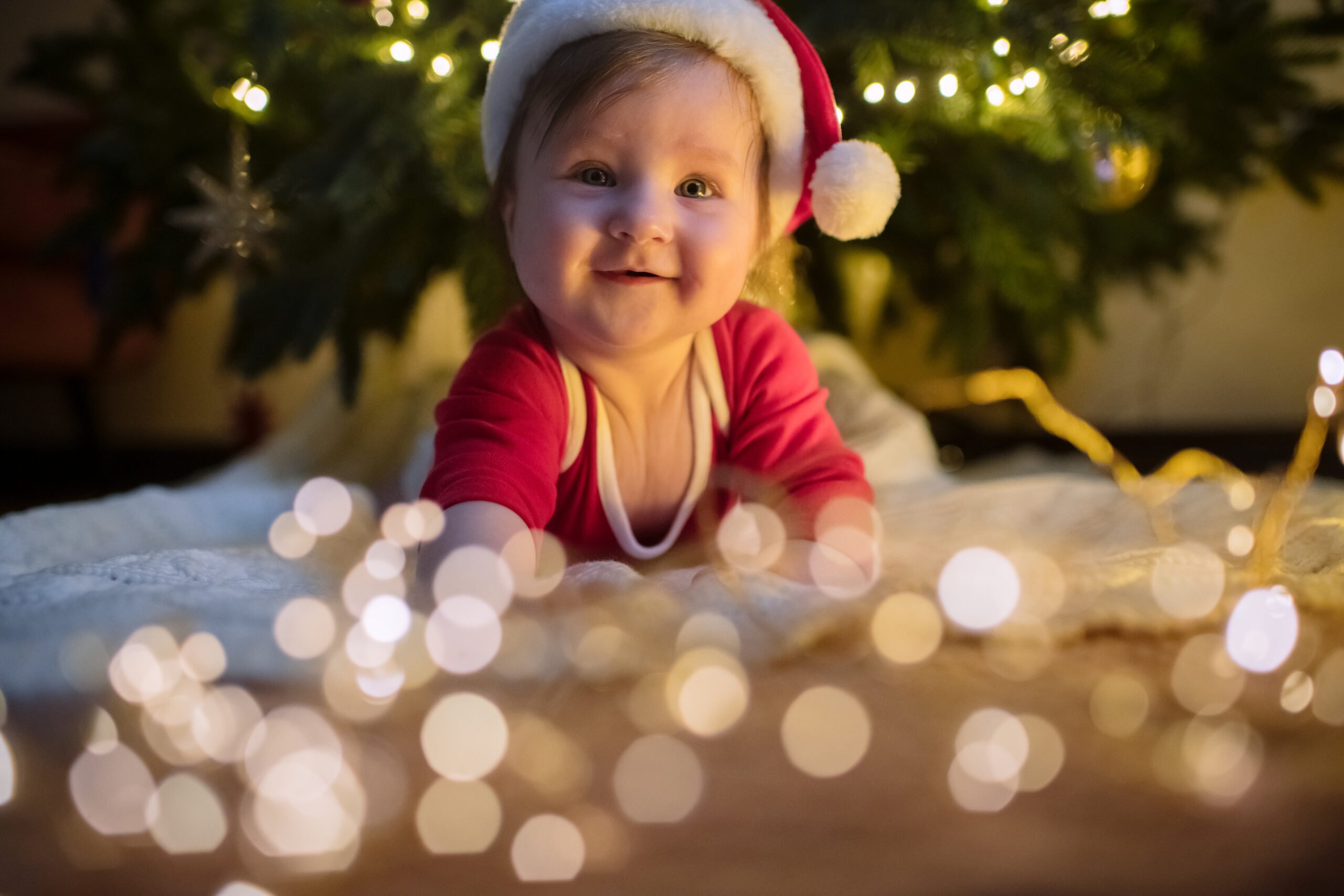 Cute baby girl in Santa hat near Christmas tree