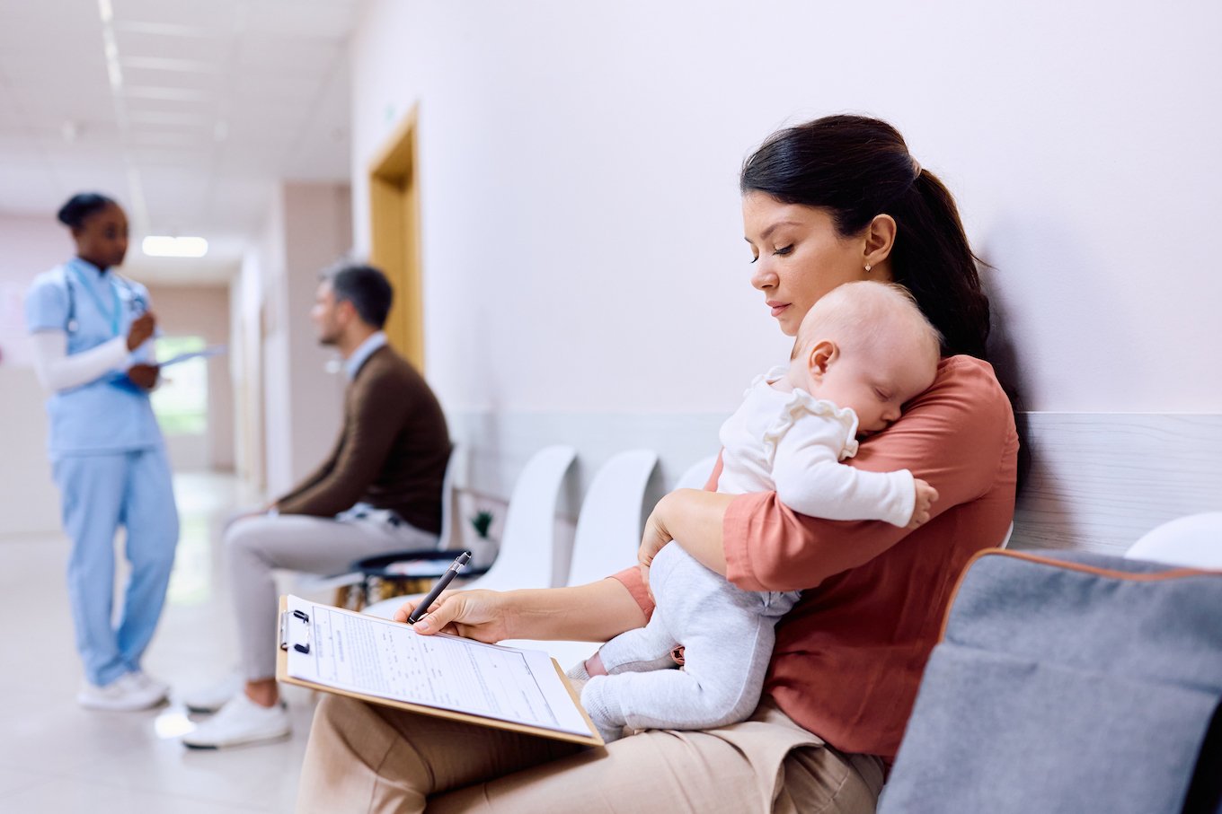 Single mother with baby filling out paperwork in waiting room at pediatrician's.