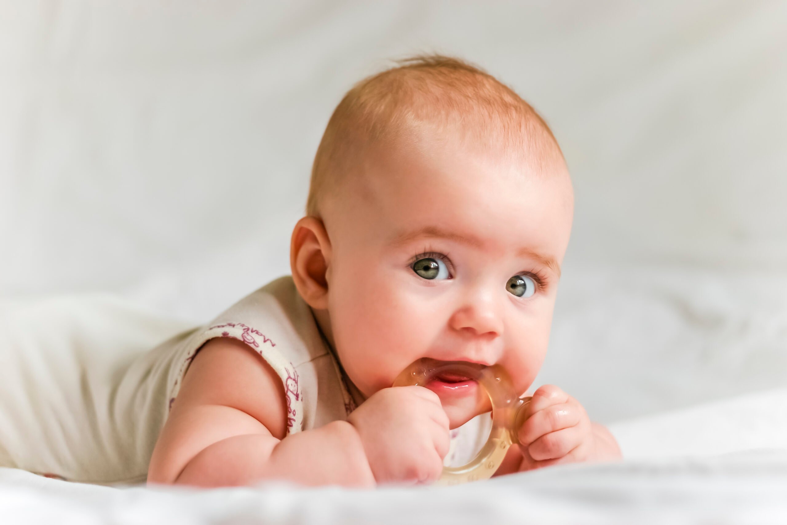 Baby girl on her stomach with teether in the mouth
