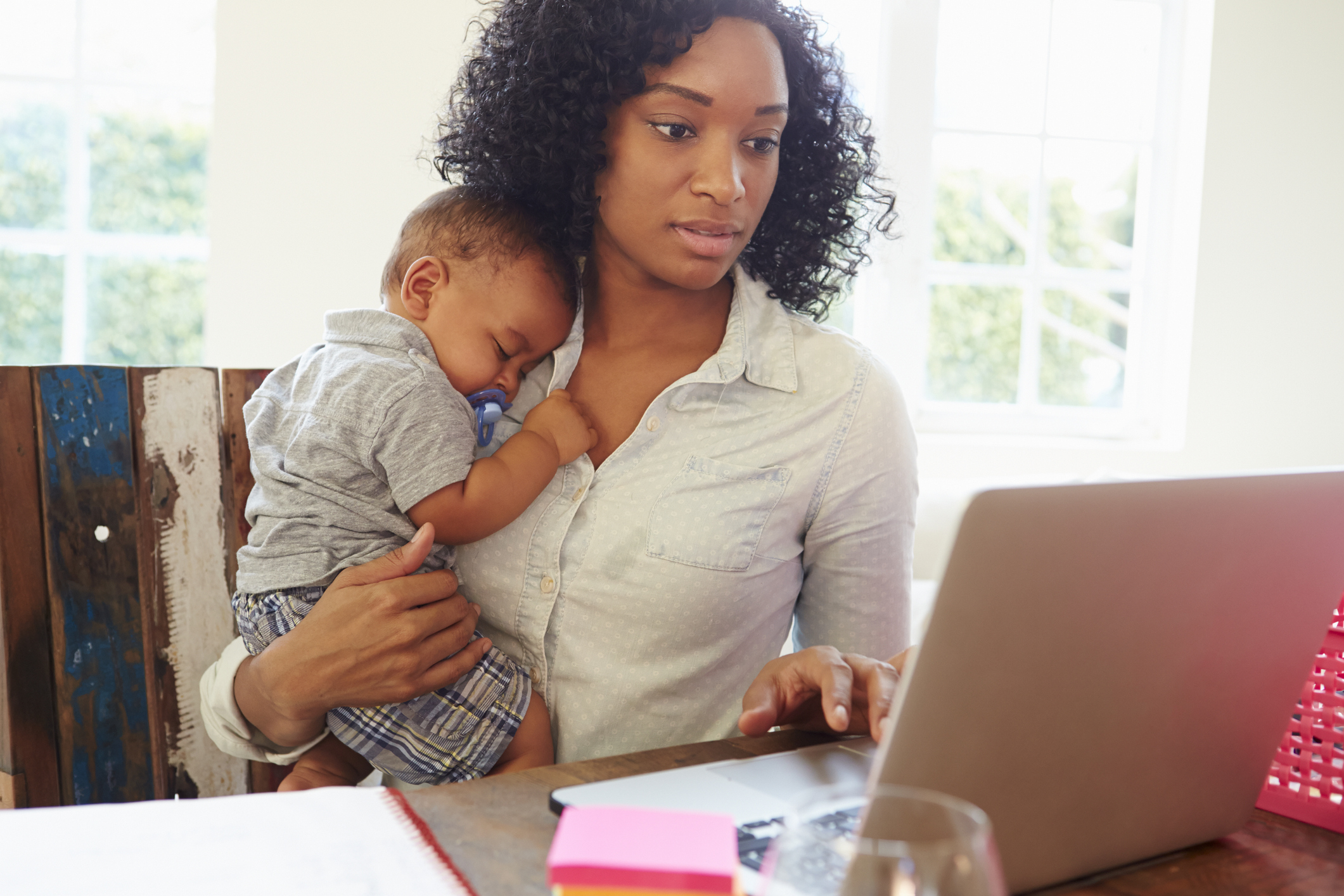 Black mom holding baby while typing on laptop