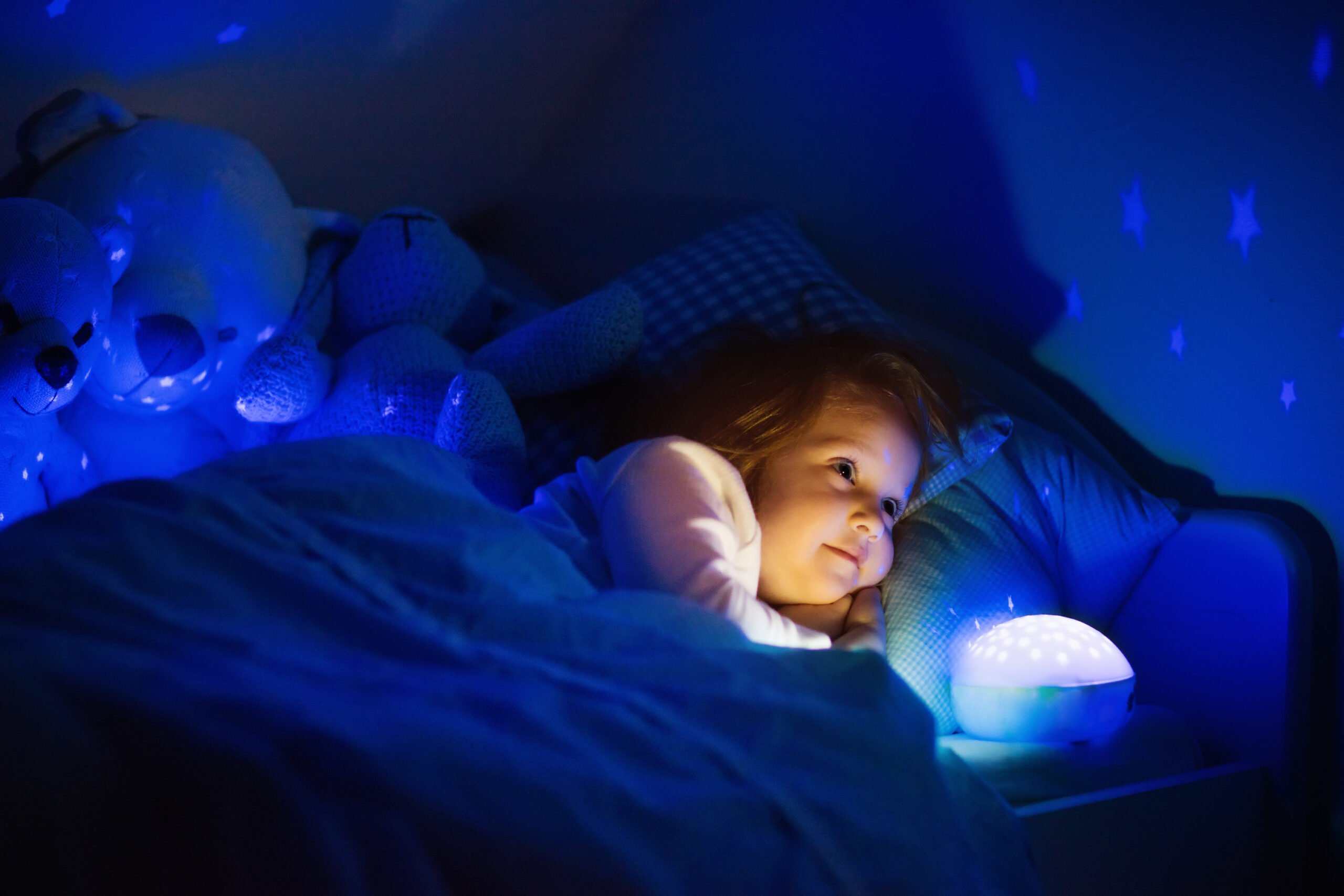 Little girl in bed with night lamp in dark nursery