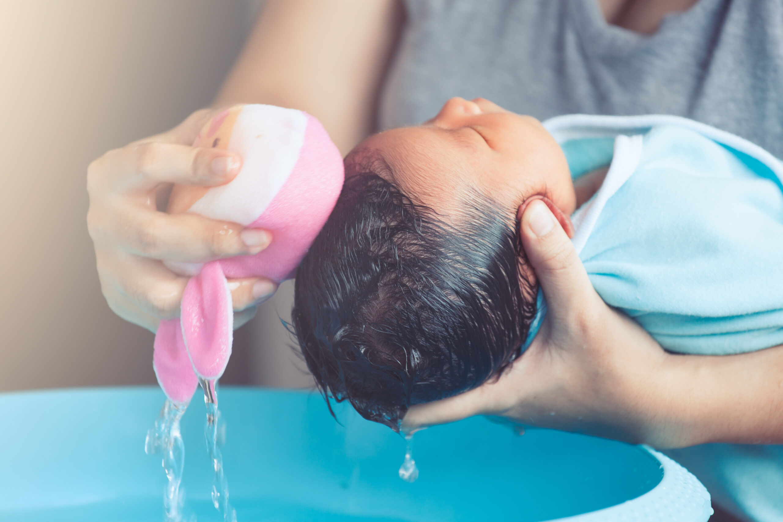 Cute asian newborn baby girl take a bath. Mom cleaning her baby hair with sponge